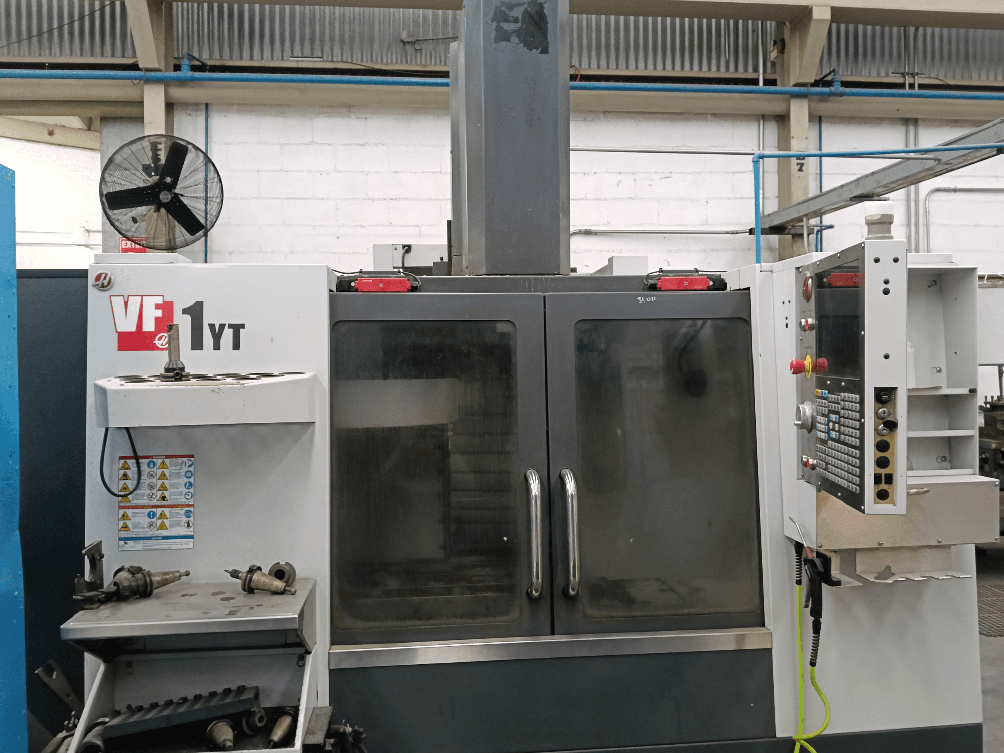 HAAS VF-1YT-1 vertikālā apstrādes centra skats no priekšpuses ar vadības paneli un instrumentiem sānos.