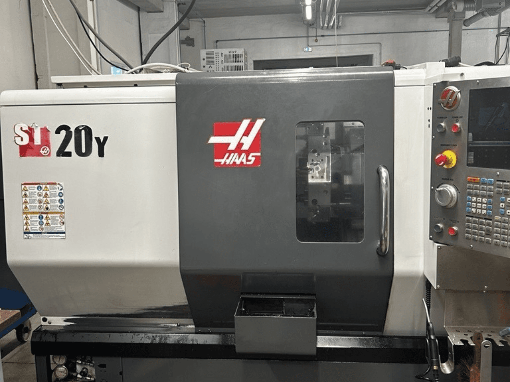 Haas ST-20Y CNC virpa, priekšējais skats, kurā redzams vadības panelis, drošības uzlīmes un darbības logs.