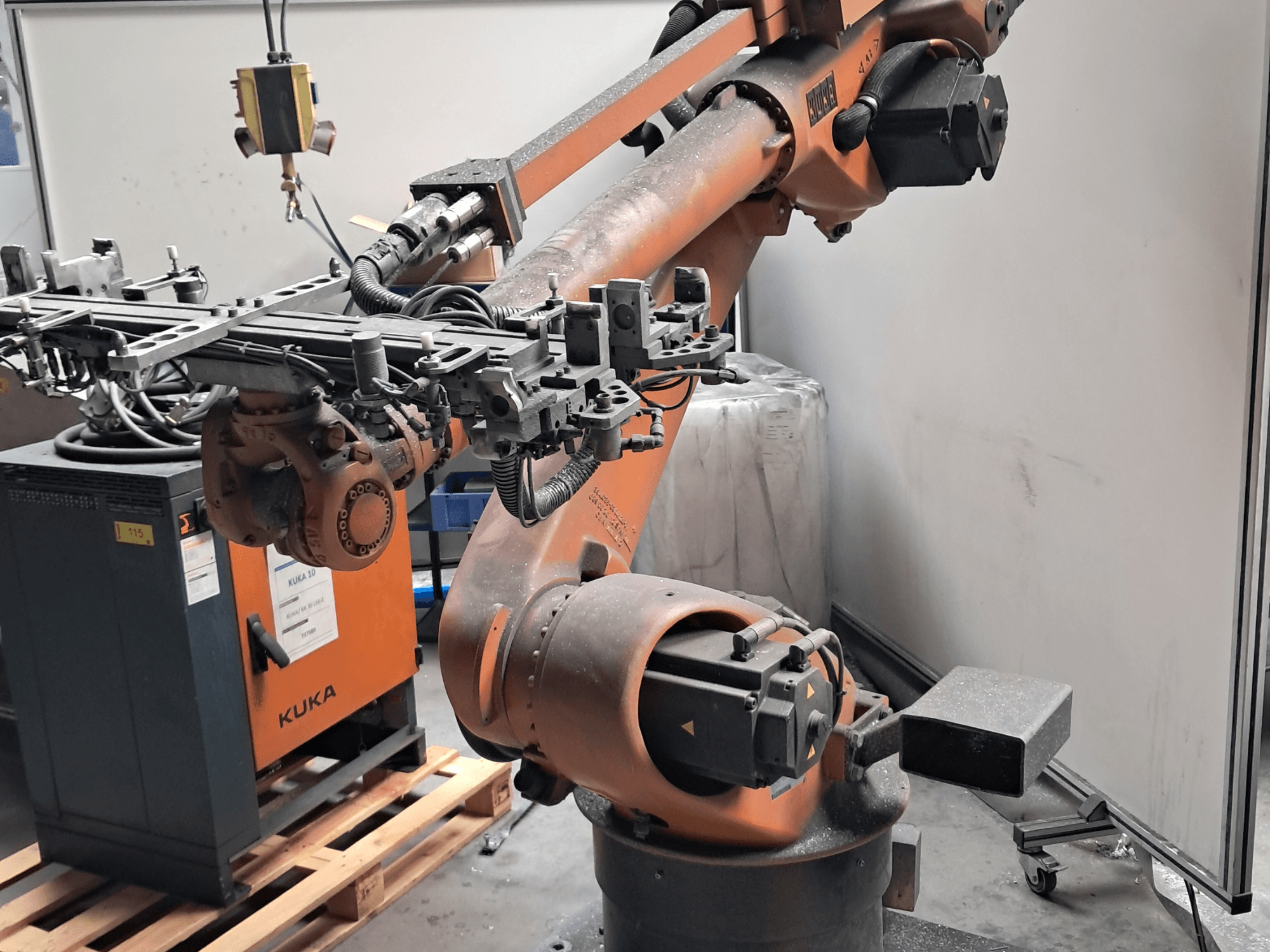 KUKA KR 30L16-2 robota roka sānskatā, ar sarežģītu darba galviņu un vadības kabeļiem, novietota blakus KUKA vadības blokam.