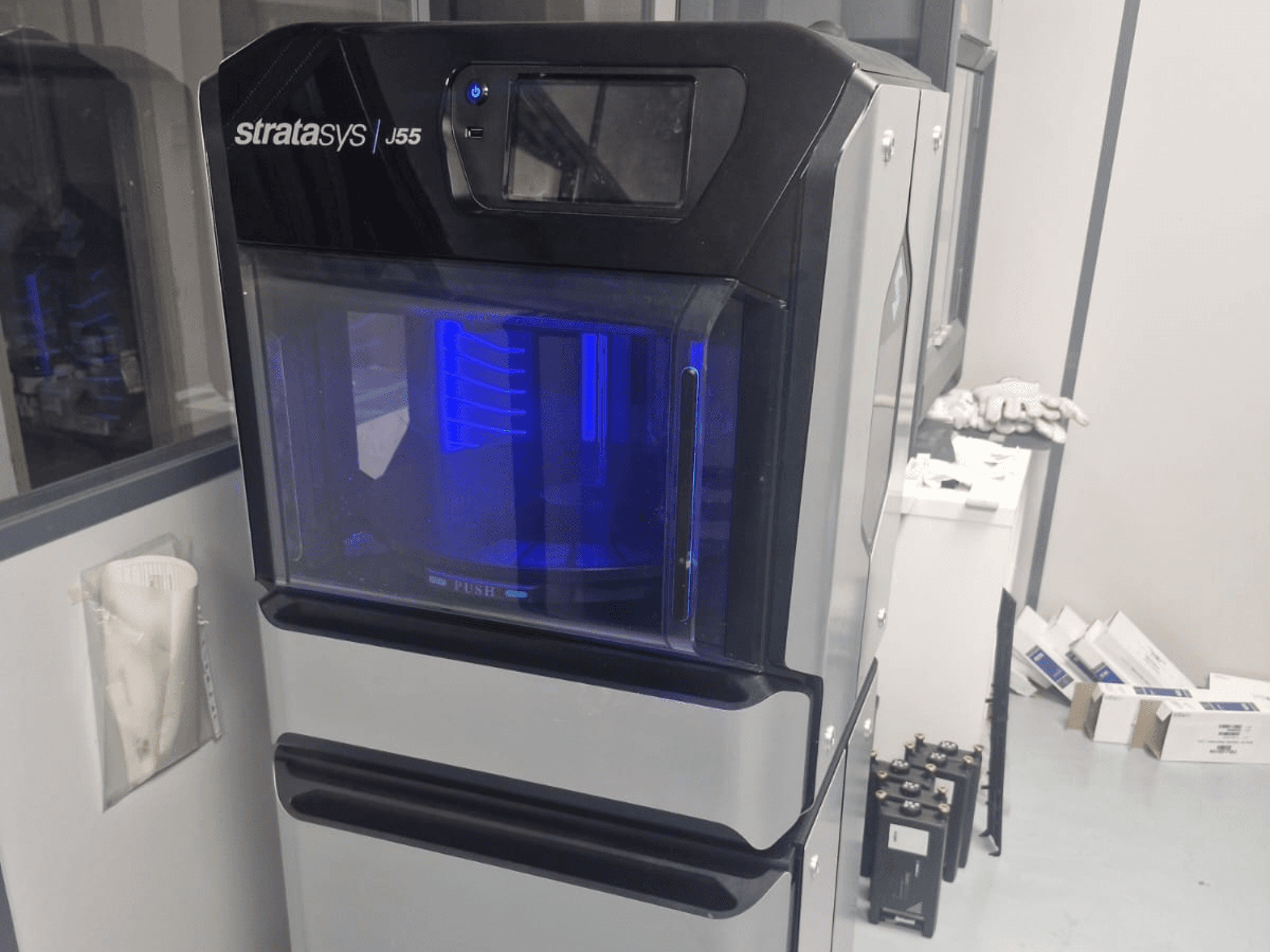 Plastmasas 3D printeris Stratasys J55 Prime no sānu skata, kurā redzams tā gludais dizains un izgaismotā drukāšanas zona.