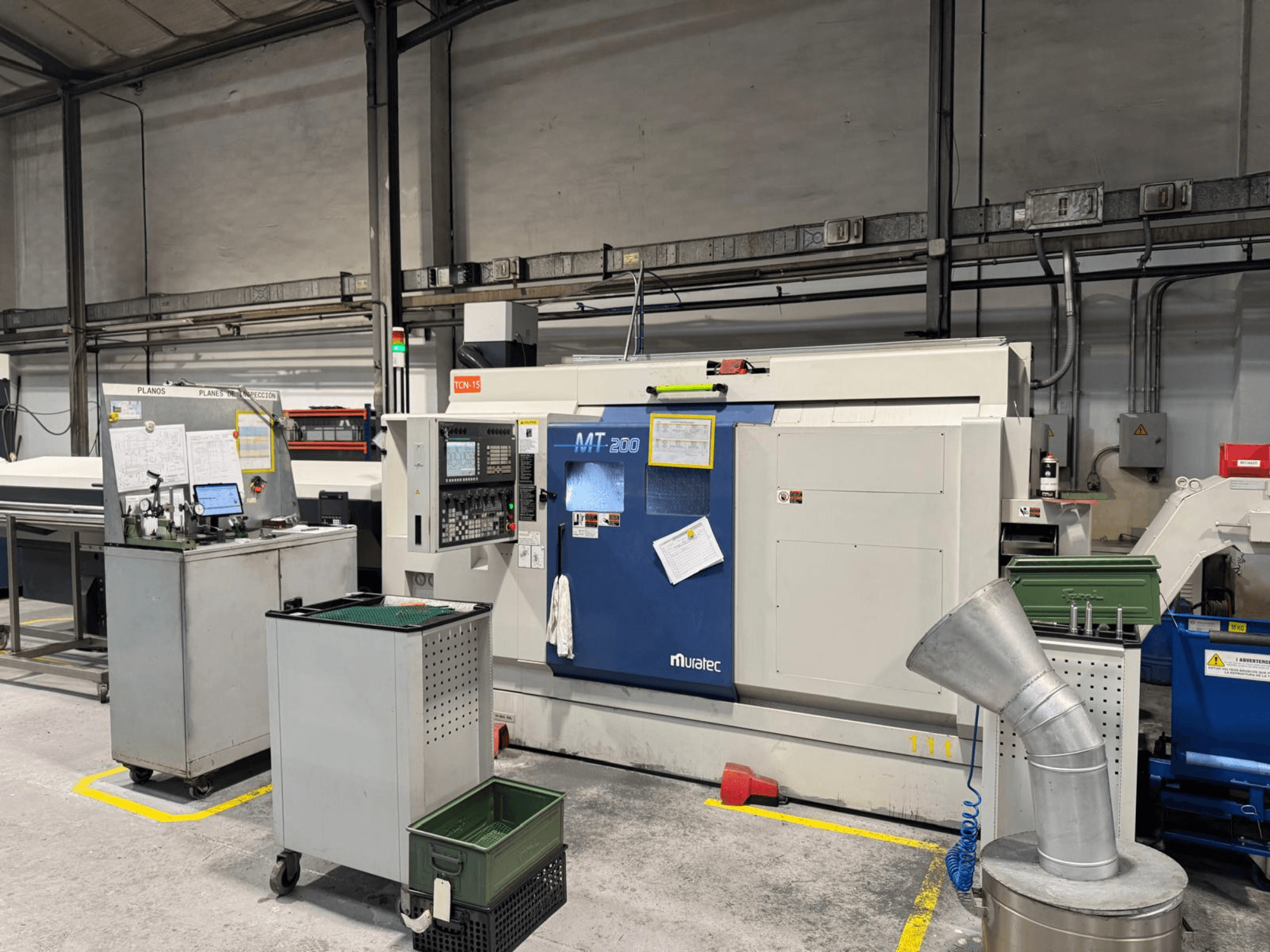 Muratec MT200 daudzvērpstu virpošanas mašīna rūpnīcā, skatoties no priekšpuses, ar vadības paneli un apkārtējām iekārtām.