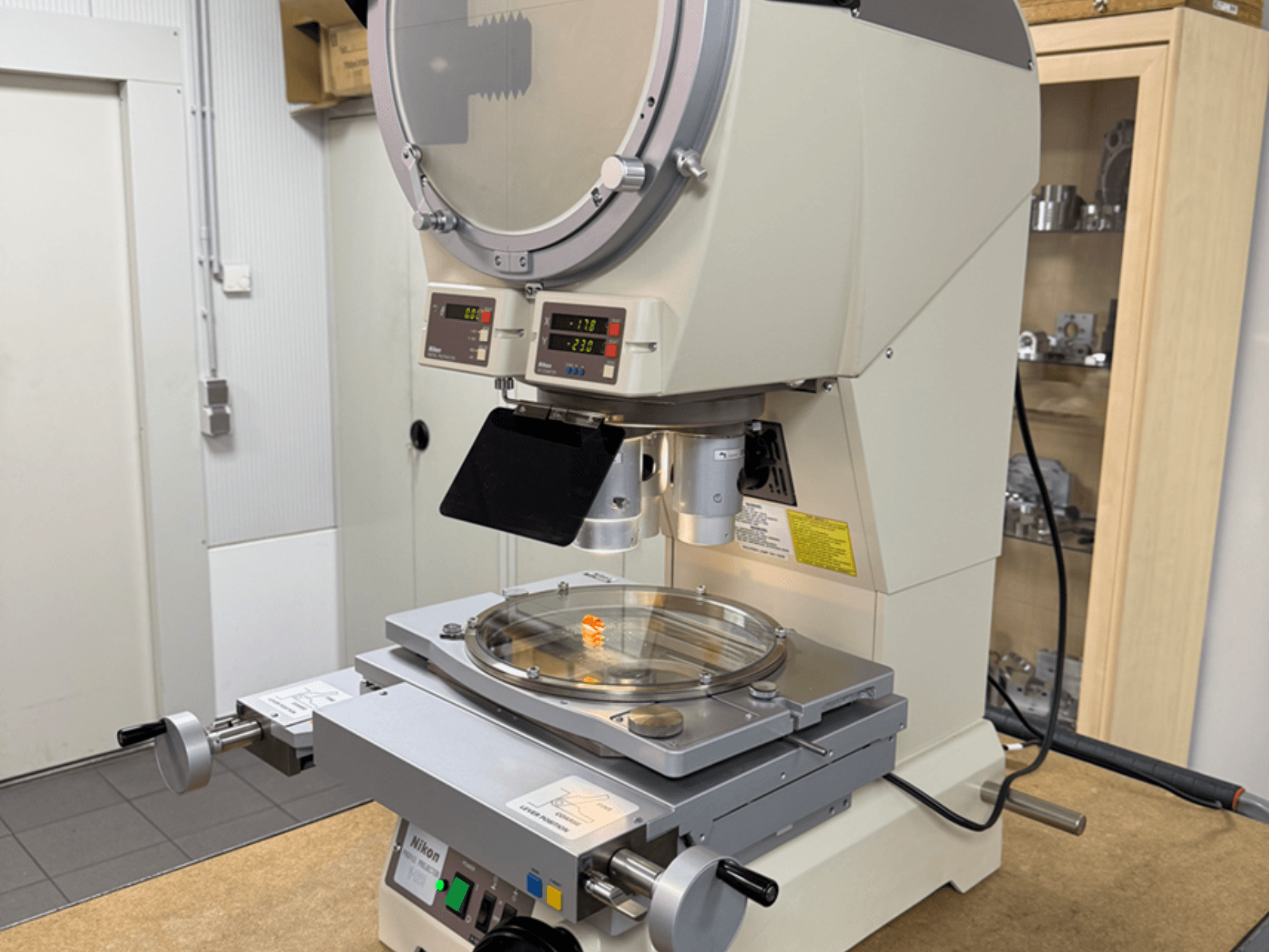Nikon modeļa mikroskops no priekšpuses, ar digitālo displeju, regulējamu statīvu un apaļu stikla plāksni.