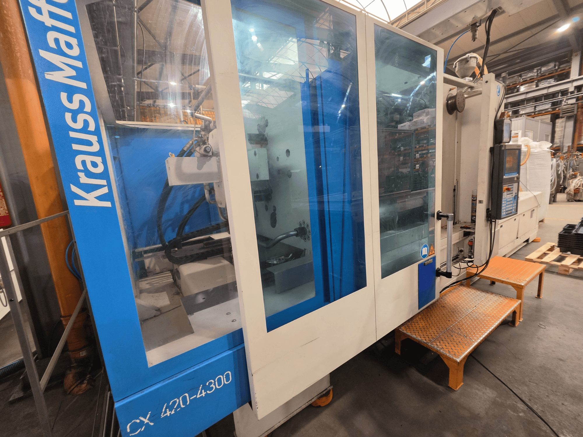 Krauss Maffei CX 420-4300 hidrauliskā iesmidzināšanas iekārta, skats no sāniem, redzams vadības panelis un caurspīdīgie paneļi.
