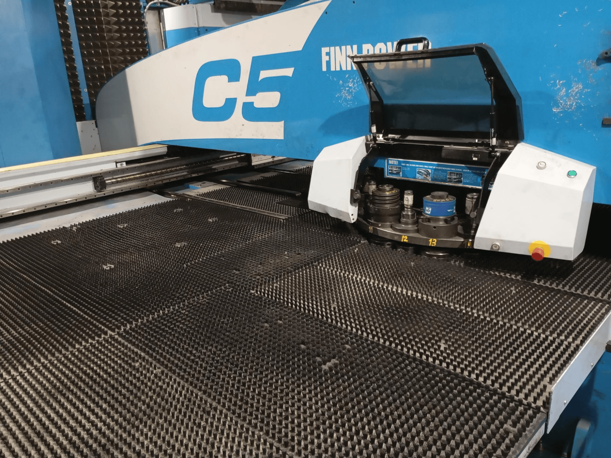 Finn-Power C5 perforatora prese, priekšējais skats, kurā redzama atvērta instrumentu galva virs teksturēta darba galda ar numurētiem indeksācijas punktiem.