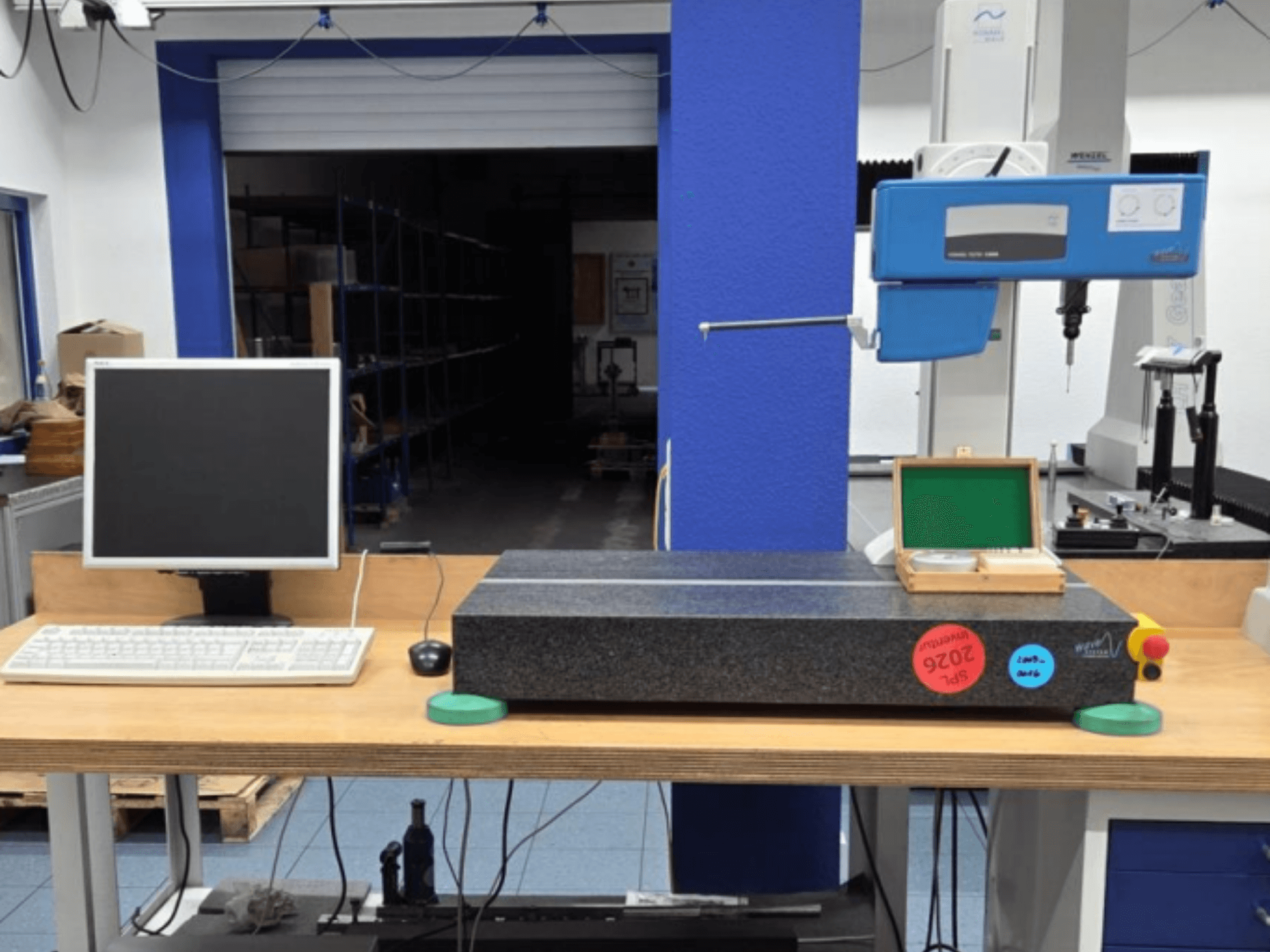 JENOPTIK wave C8000 CMM darbnīcā ar monitoru, tastatūru un granīta mērīšanas virsmu. Skats no priekšpuses.