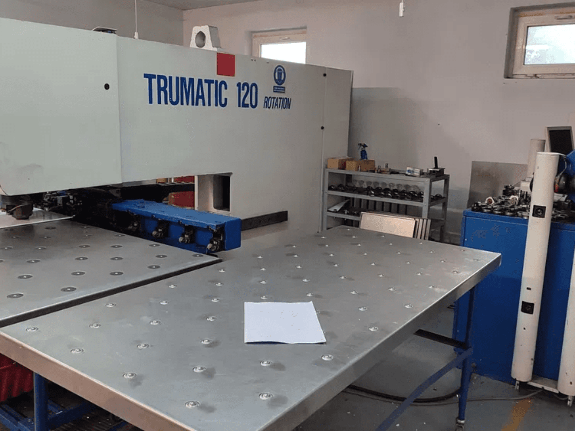 TRUMPF TRUMATIC 120R CNC caurumošanas iekārta TRUMPF TRUMATIC 120R, skatoties no priekšpuses, ar metāla galdu ar caurumiem un tukšu lapu.