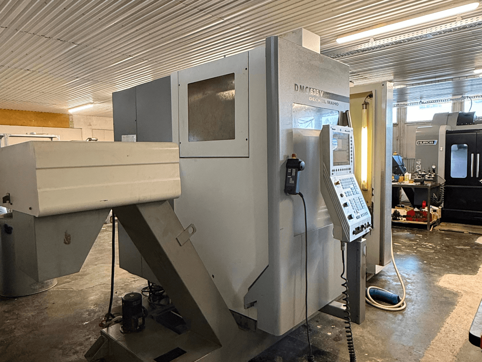 DMC G635V frēzēšanas iekārta darbnīcā, priekšējais skats ar redzamu vadības paneli un pievienotajiem elektroinstrumentiem.