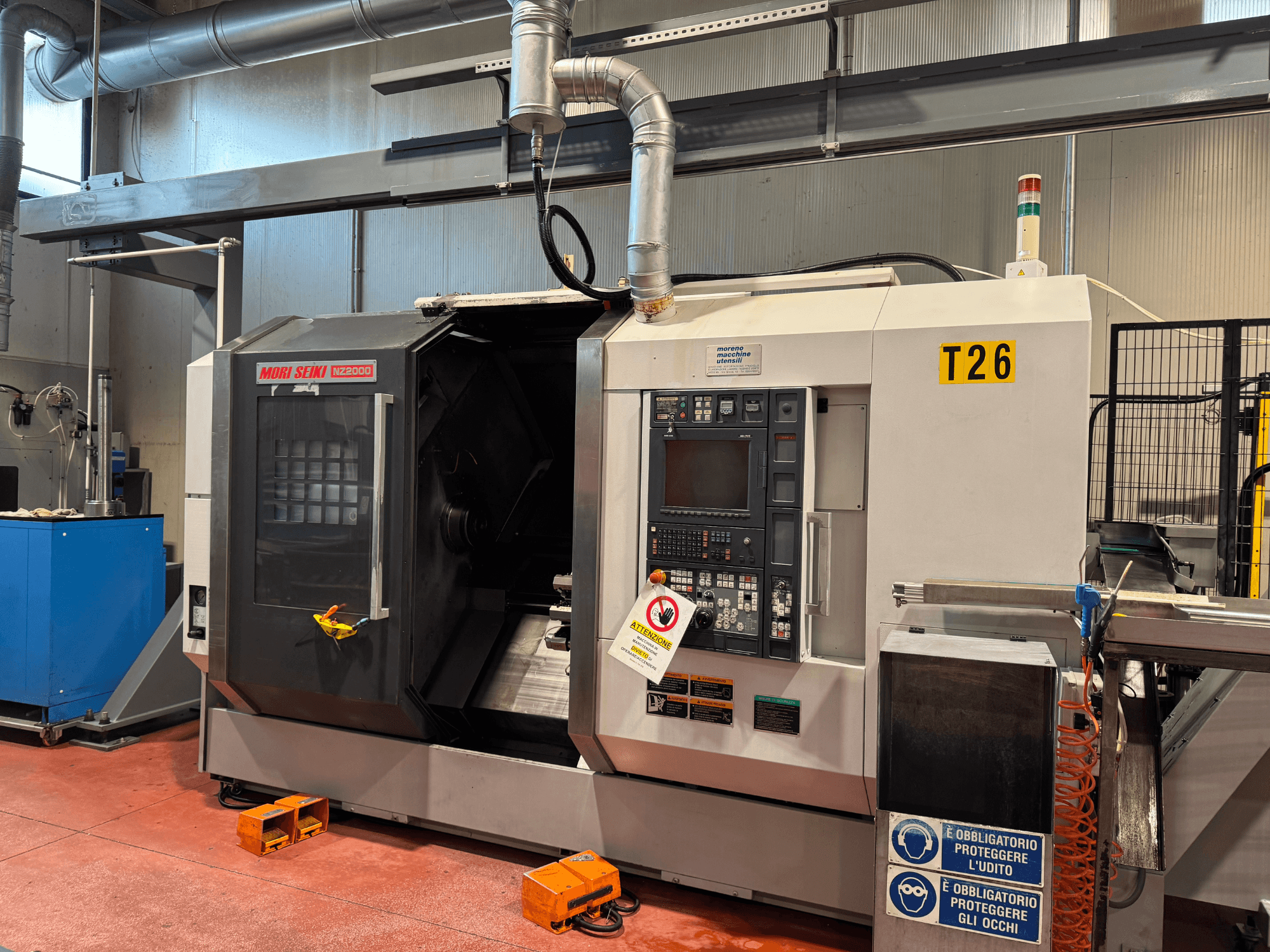 MORI SEIKI NZ-2000/T2/Y2 rotācijas frēzēšanas centrs, skats no priekšpuses, ar vadības paneli, drošības zīmēm un rūpniecisko iestatījumu.