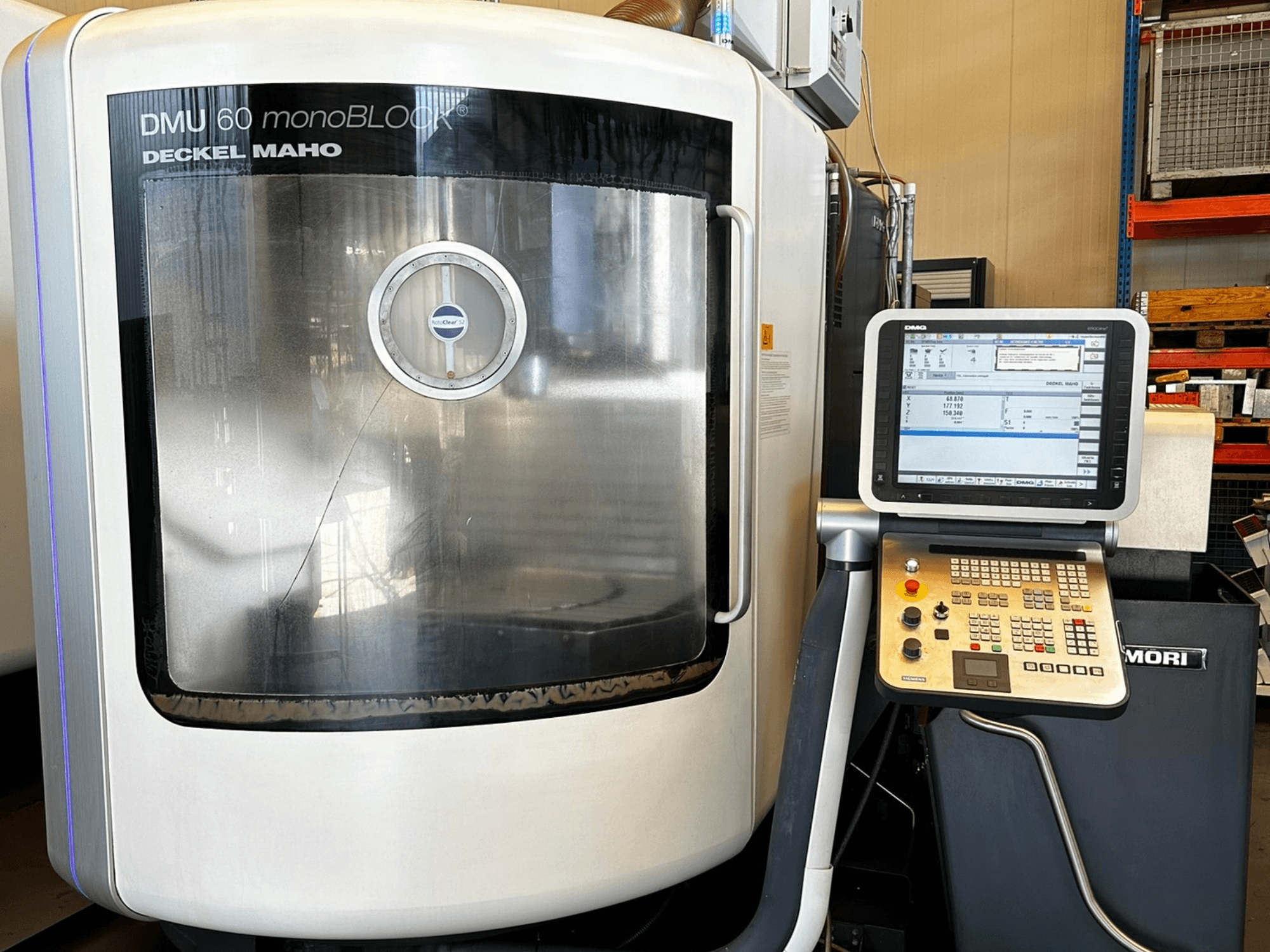 DMG MORI DMU 60 monoBLOCK vertikālais apstrādes centrs, skats no priekšpuses, ar skārienjūtīgo vadības paneli un atstarojošo logu.