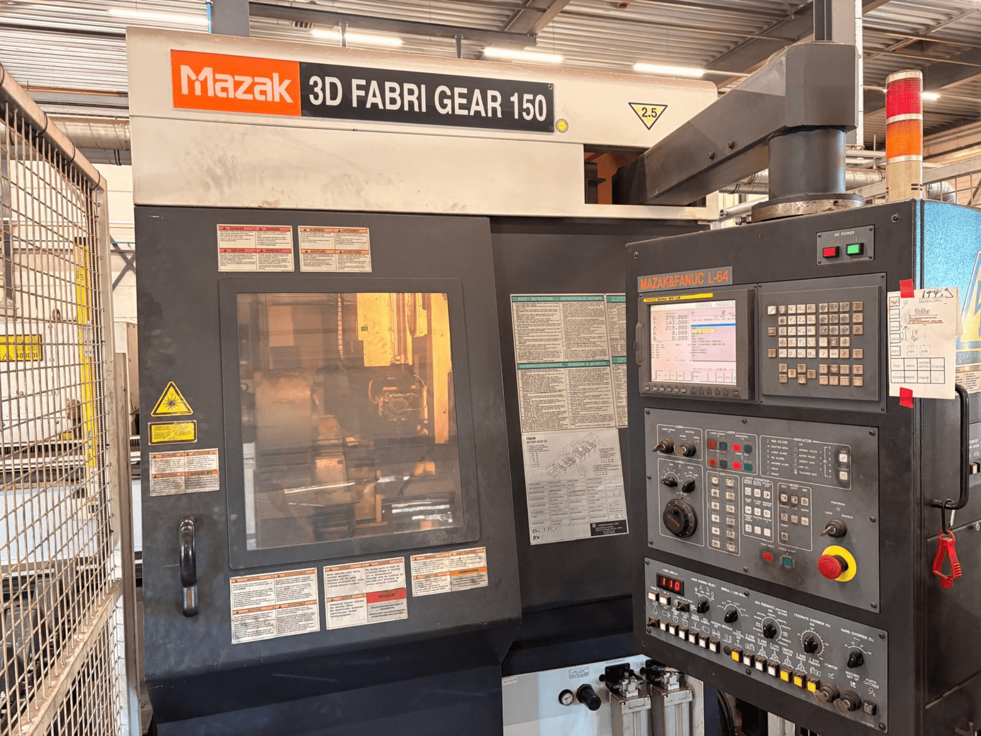 Mazak 3D Fabri Gear 150 cauruļu griešanas mašīna, skats no priekšpuses, kurā redzams vadības panelis, drošības uzlīmes un darbības interfeiss.