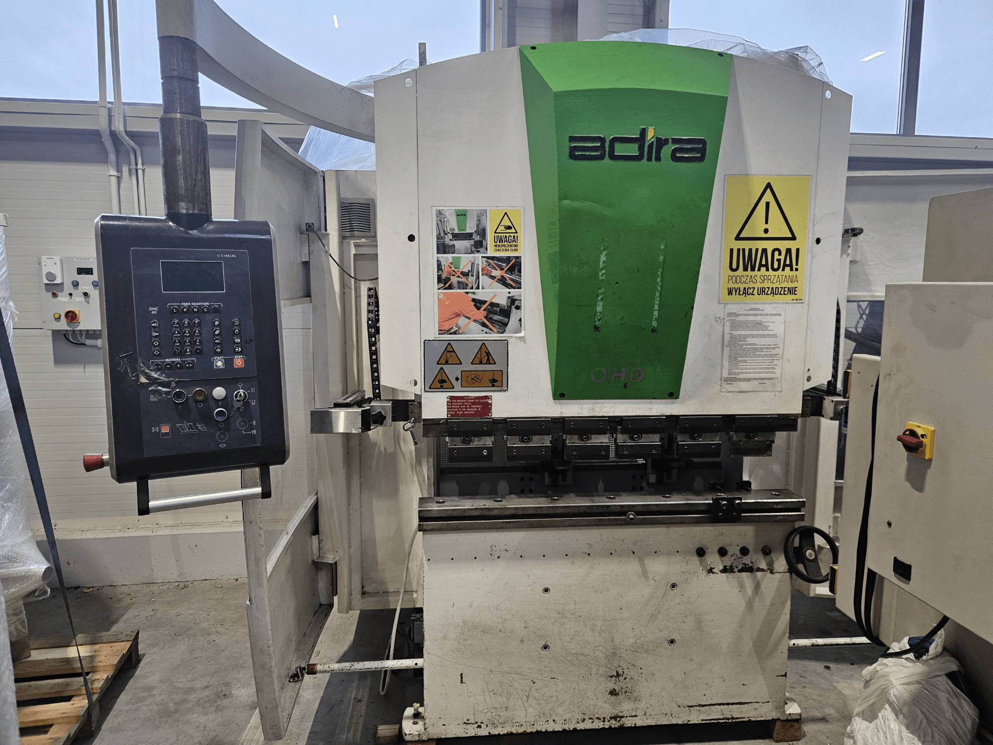 Adira OHD mašīna no priekšpuses, ar vadības paneli, drošības brīdinājumiem un darbības pogām.