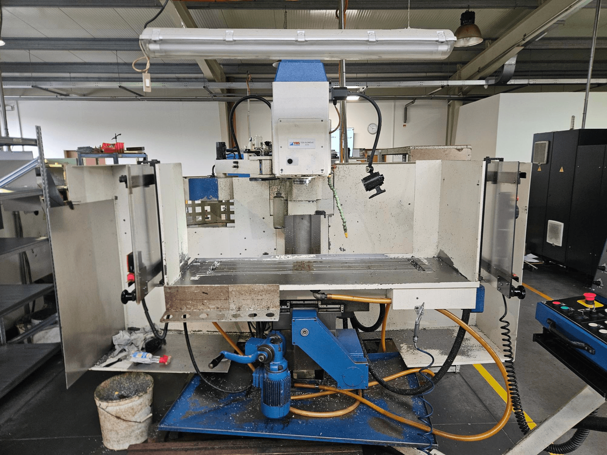 TOS Olomouc FV30 CNC Vertikālais apstrādes centrs darbnīcā, priekšējais skats, kurā redzams vadības panelis, darba galds un dzesēšanas sistēma.