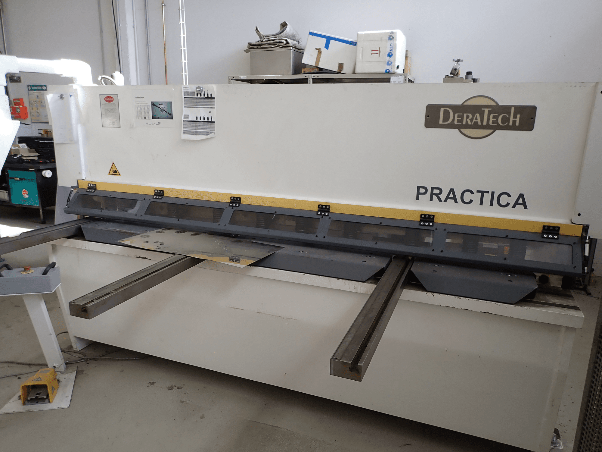 DERATECH Practica CNC šķēres, skats no priekšpuses, redzams griešanas asmens un metāla loksnes uz darba virsmas.