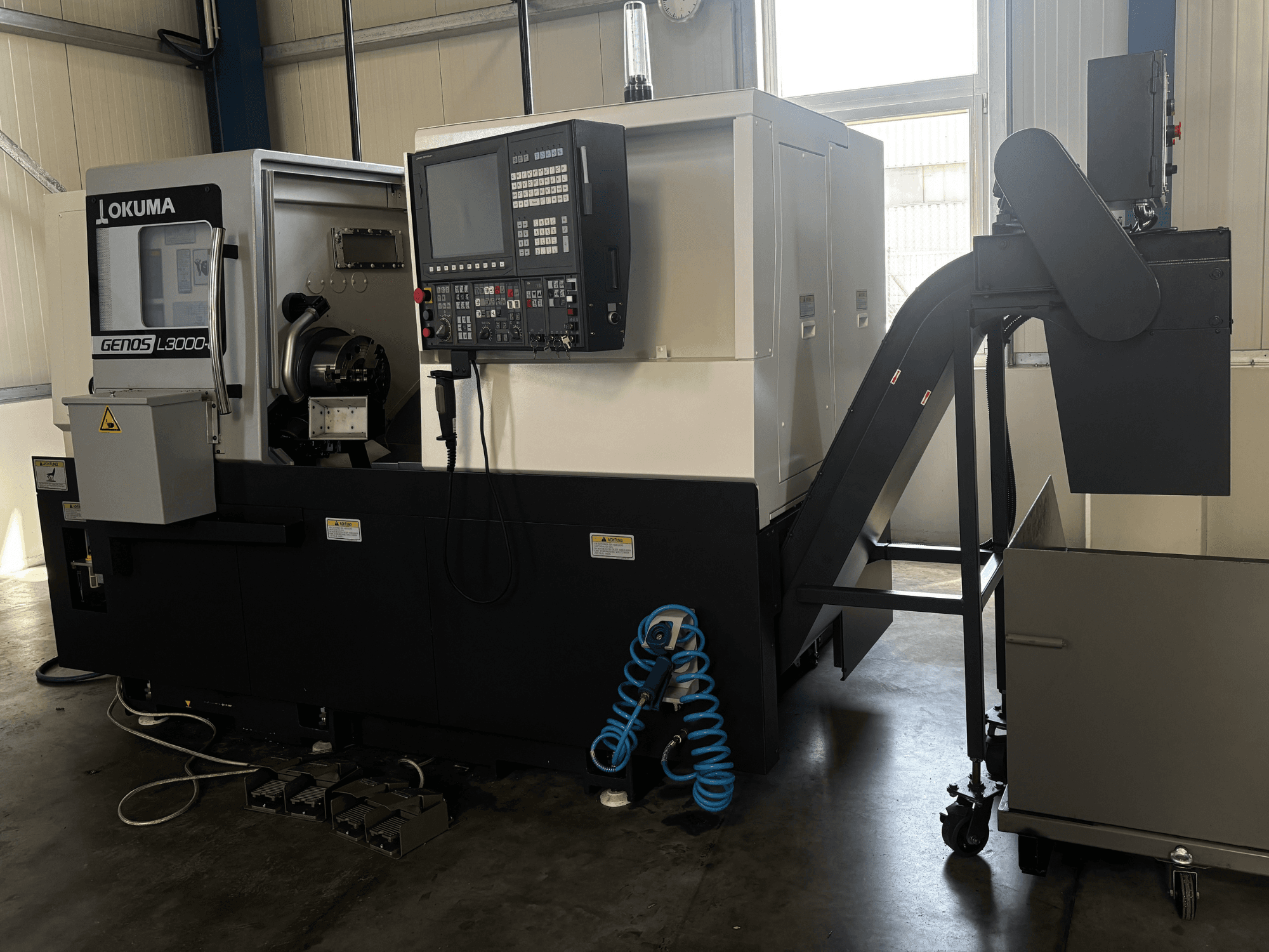 Okuma GENOS L3000-e horizontālā virpošanas mašīna, skats no priekšpuses, kurā redzams vadības panelis, konveijers un vārpstas zona.