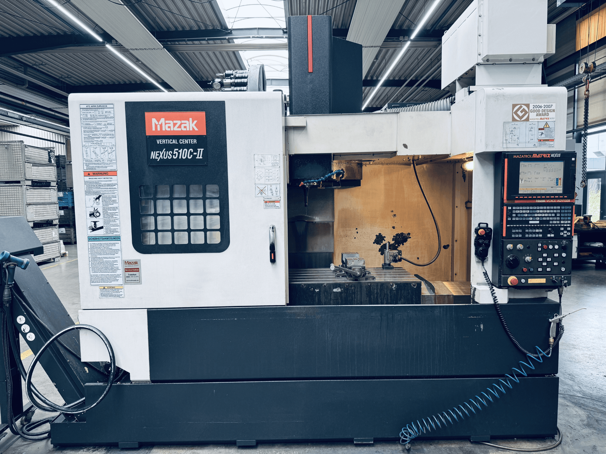 Mazak vertikālais apstrādes centrs Nexus 510C-II, skats no priekšpuses, kurā redzams vadības panelis, darba zona un darbības funkcijas darbnīcas vidē.