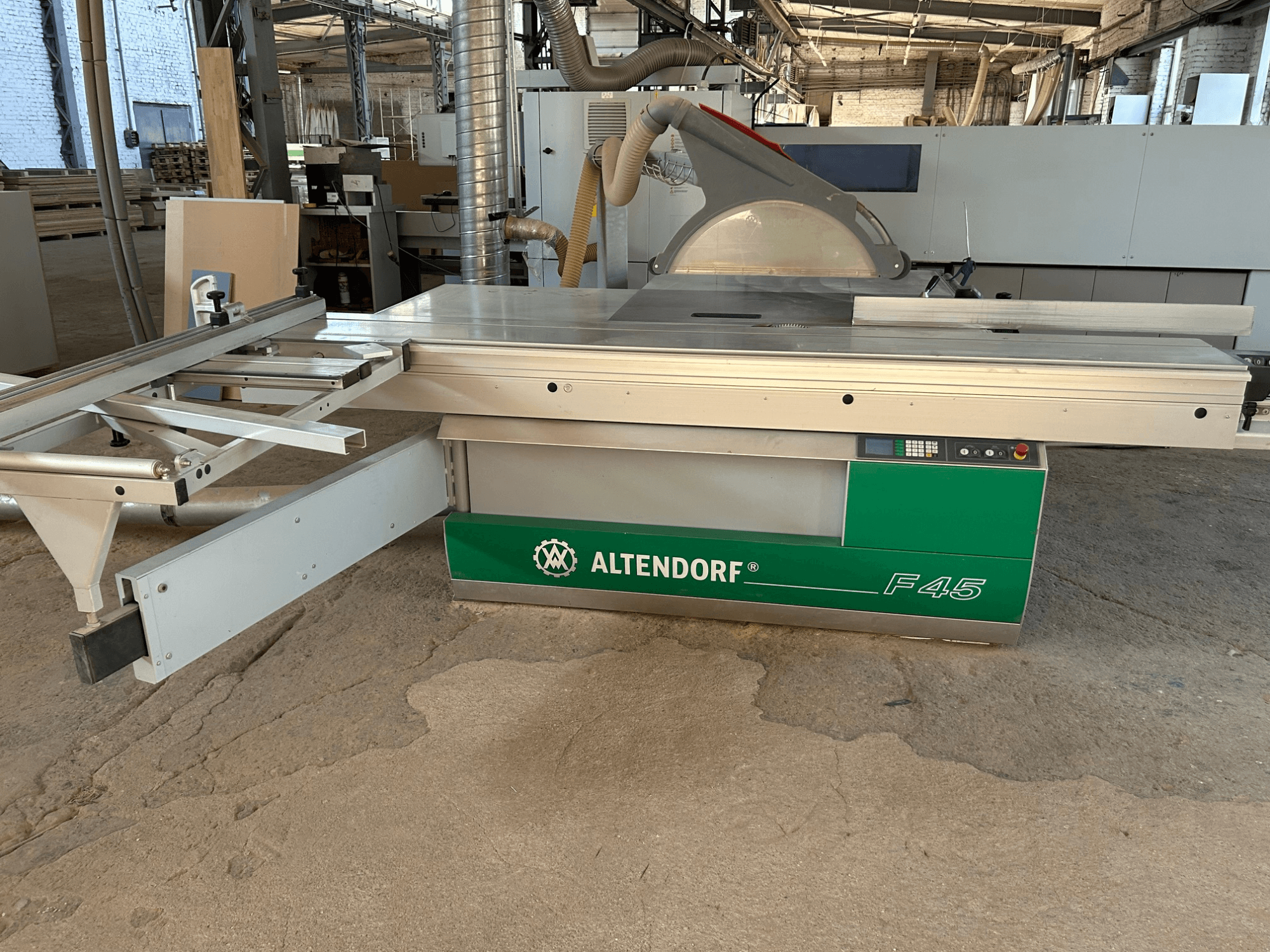 Altendorf F 45 paneļu zāģis, skats no priekšpuses, kurā redzams griešanas galds, zāģa asmens aizsargs un vadības panelis uz zaļā un pelēkā mašīnas.