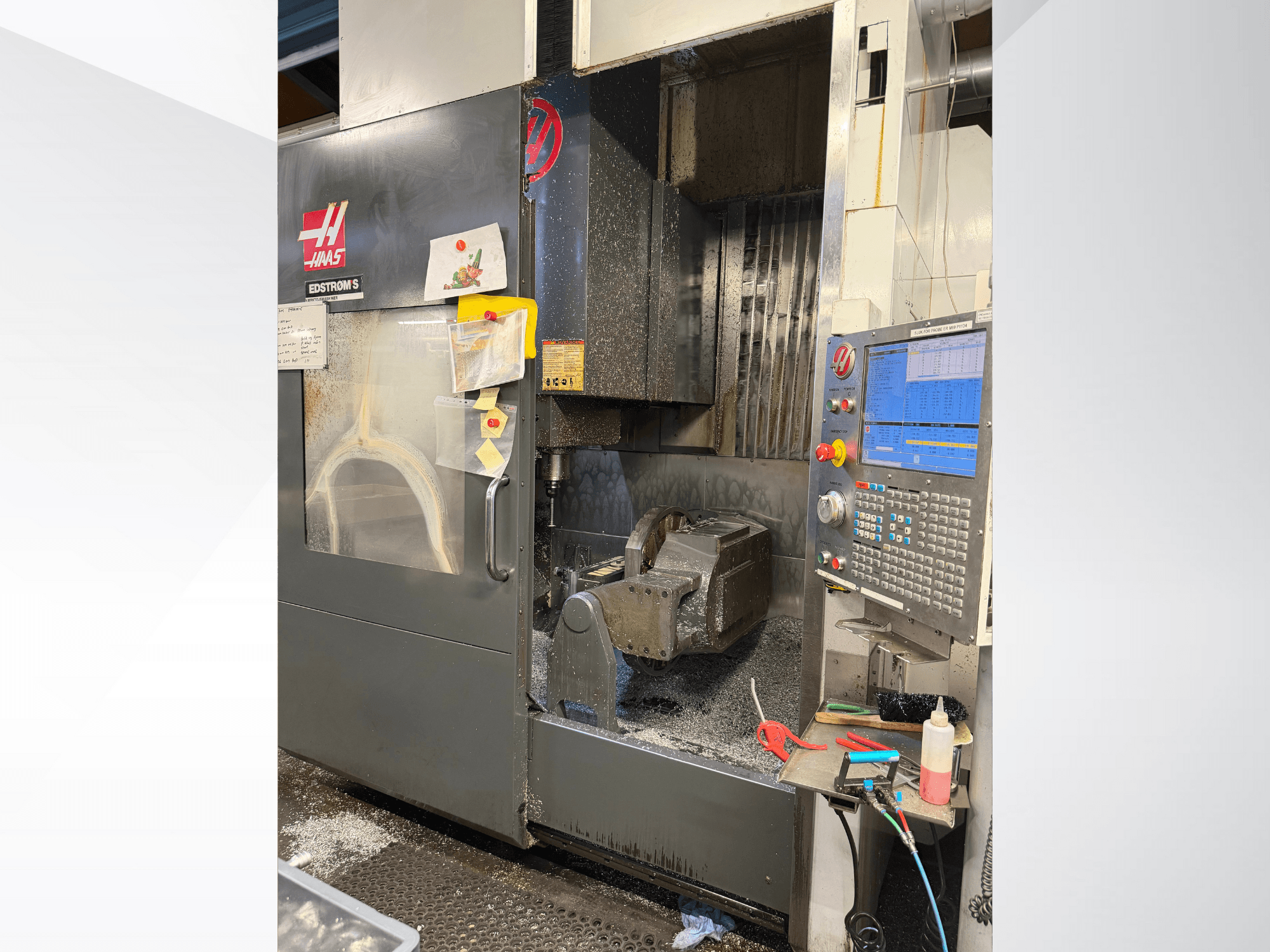 Haas CNC darbgalds, modelis EDSTROM S, skats no priekšpuses, kurā redzams metāla sagataves, vadības panelis un metāla skaidas iekšpusē.