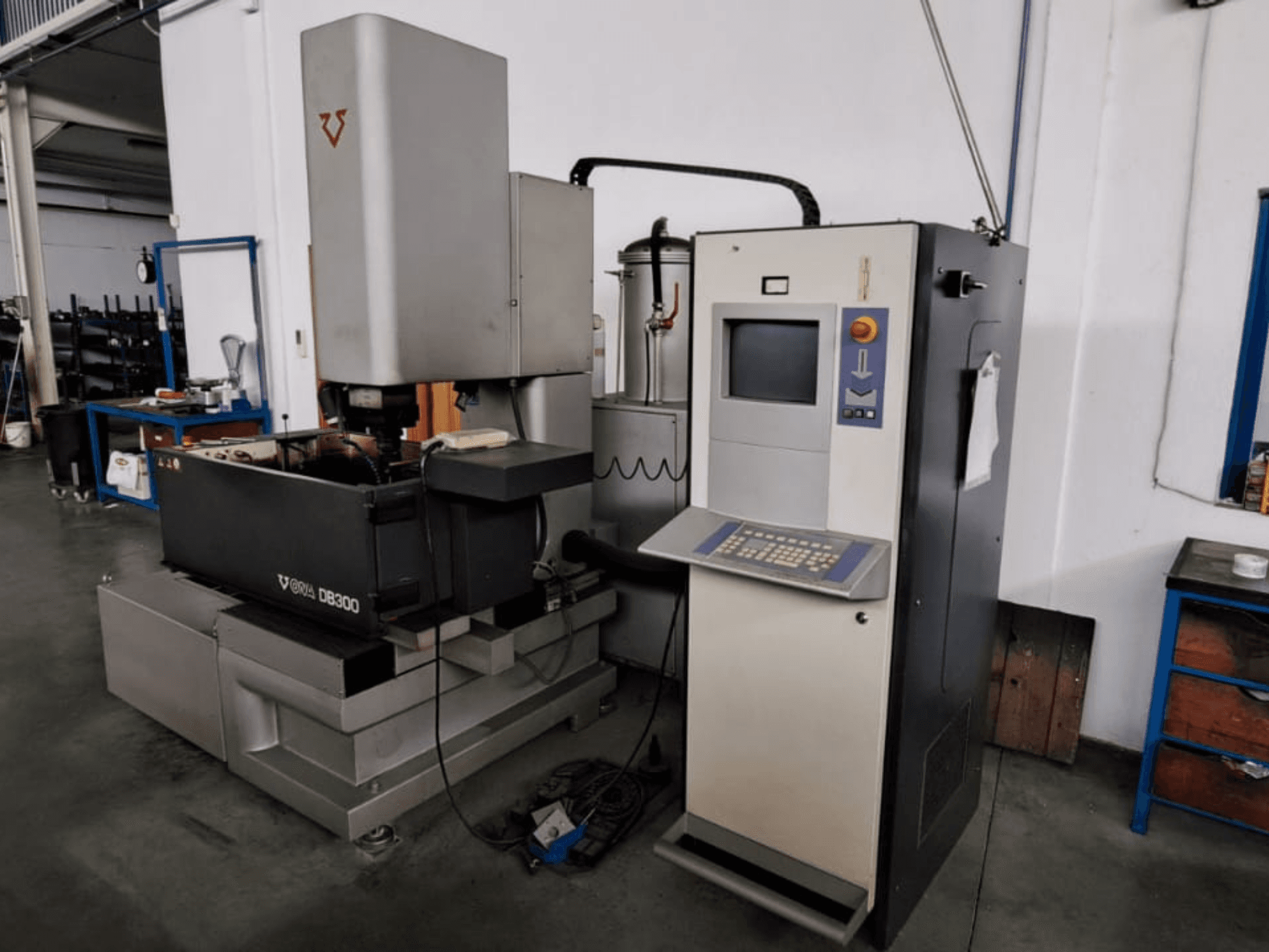 Štancēšanas EDM mašīna ONA DB300, skats no priekšpuses; ar vadības paneli, sagataves turētāju un rūpnieciskā dizaina elementiem.