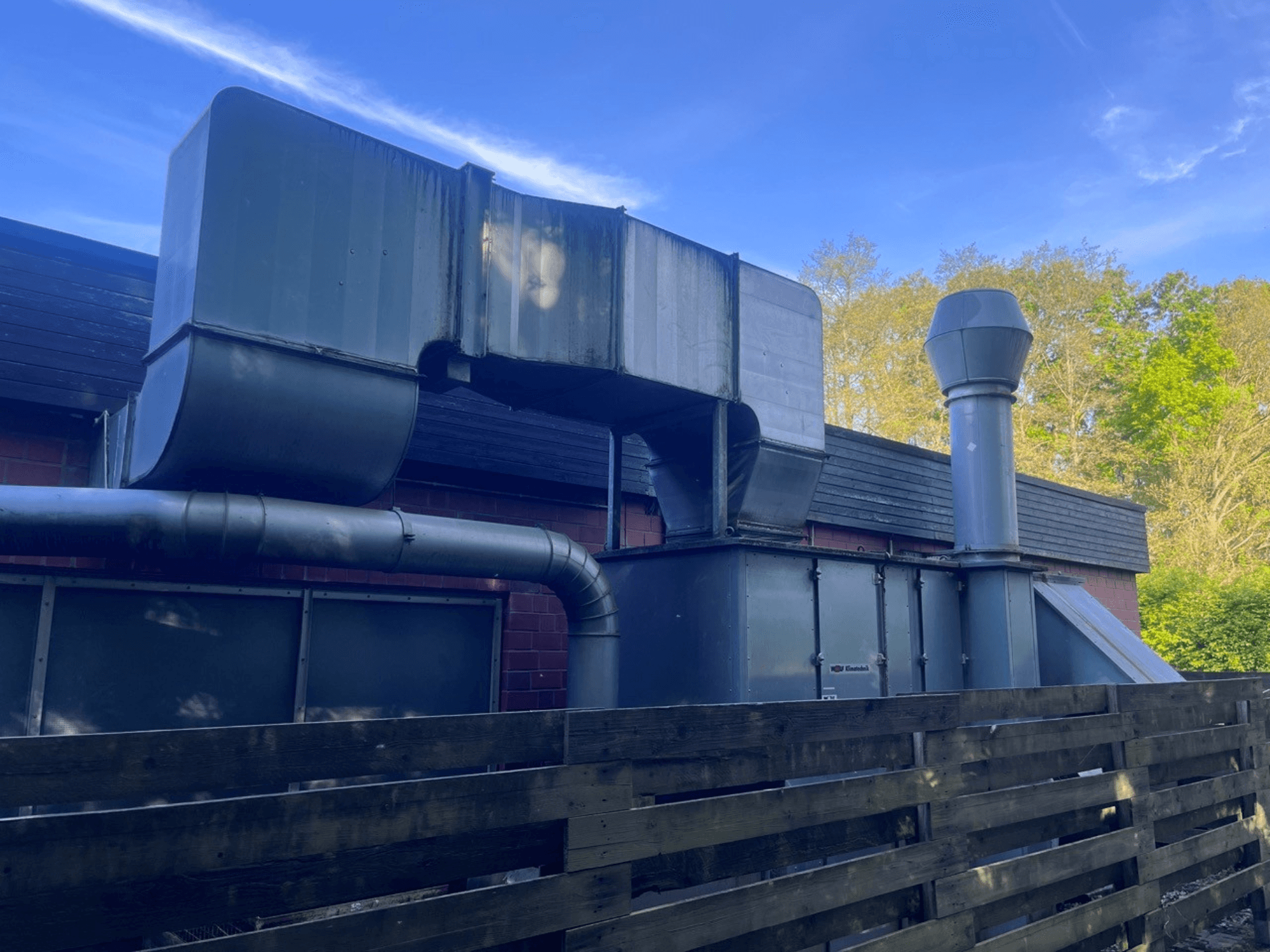 Rūpnieciskās ventilācijas sistēma ar metāla cauruļvadiem, skats no sāniem; ietver kvadrātveida un cilindrisku skursteni, zaļa apdare.