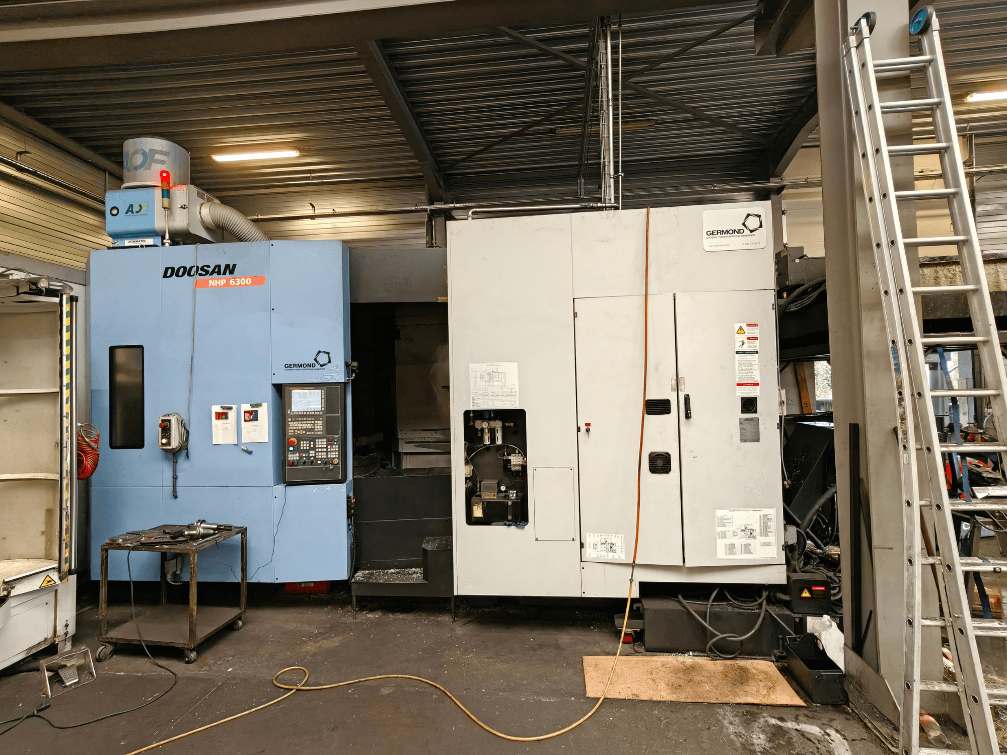 DOOSAN NHP6300 horizontālais apstrādes centrs, skats no priekšpuses, kurā redzams vadības panelis un blakus esošās iekārtas darbnīcas vidē.