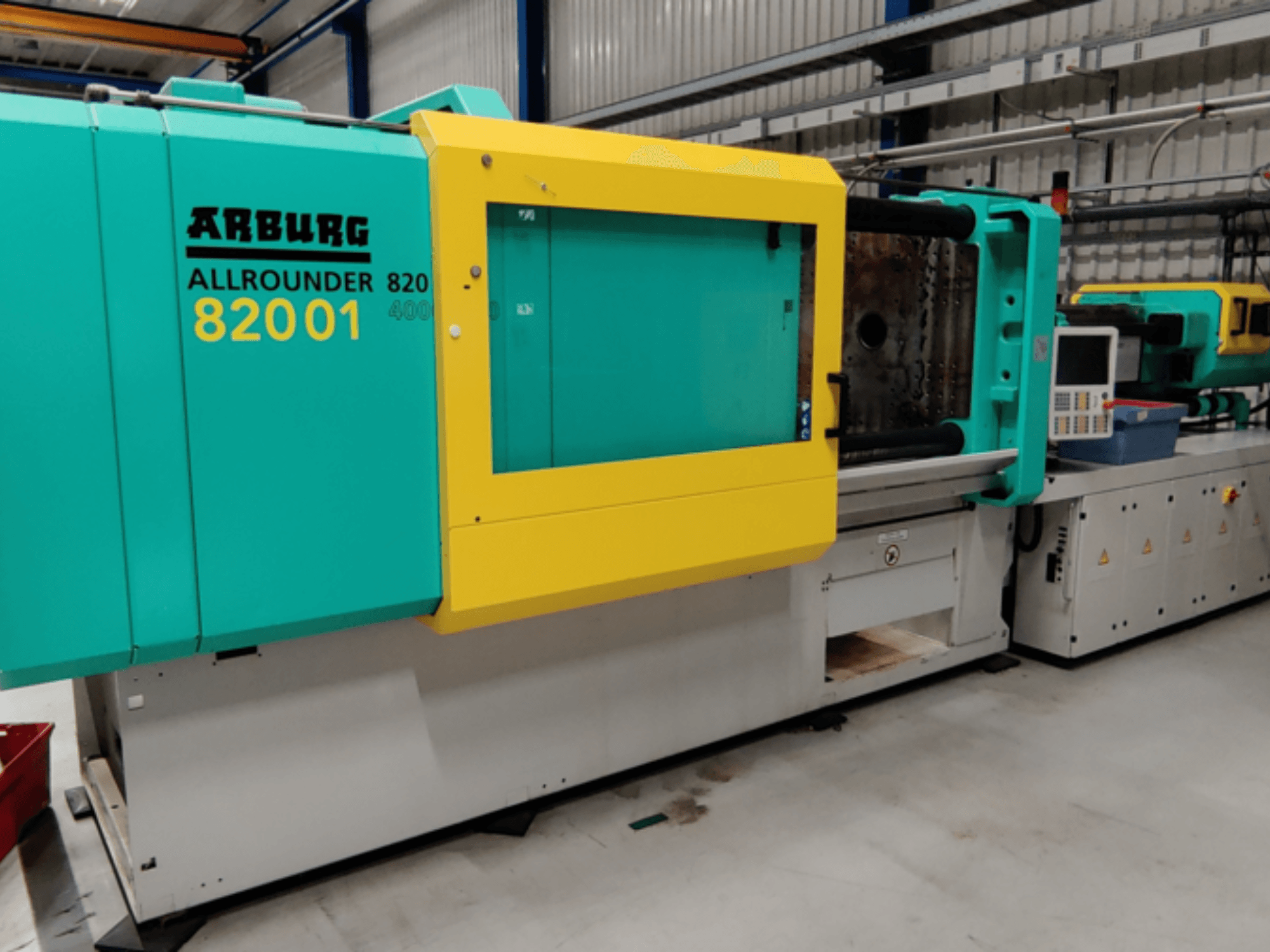 Arburg ALLROUNDER 82001 injekcijas formēšanas iekārta tīģeļu un dzeltenā krāsā, sānu skats, kurā redzams vadības panelis un darbības funkcijas.