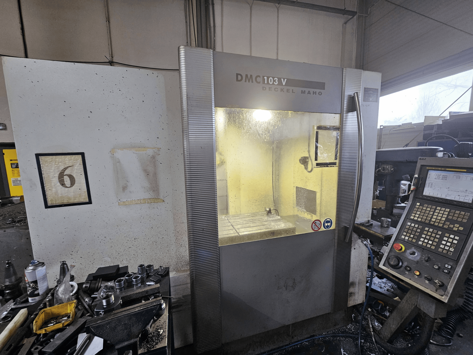 Deckel Maho DMC 103 V CNC mašīnas priekšējais skats, kurā redzams vadības panelis, darba zona un numurētais indikators "6".
