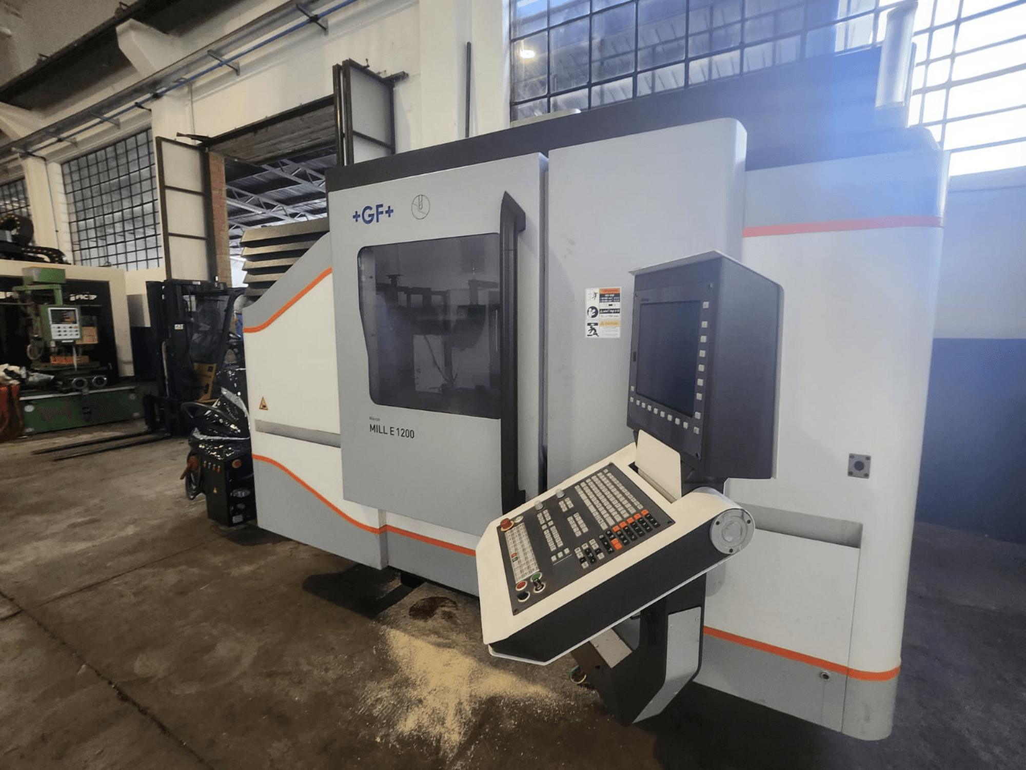 GF MILL E1200, priekšējais skats uz frēzmašīnu ar vadības paneli, displeja ekrānu un drošības marķējumu darbnīcā.