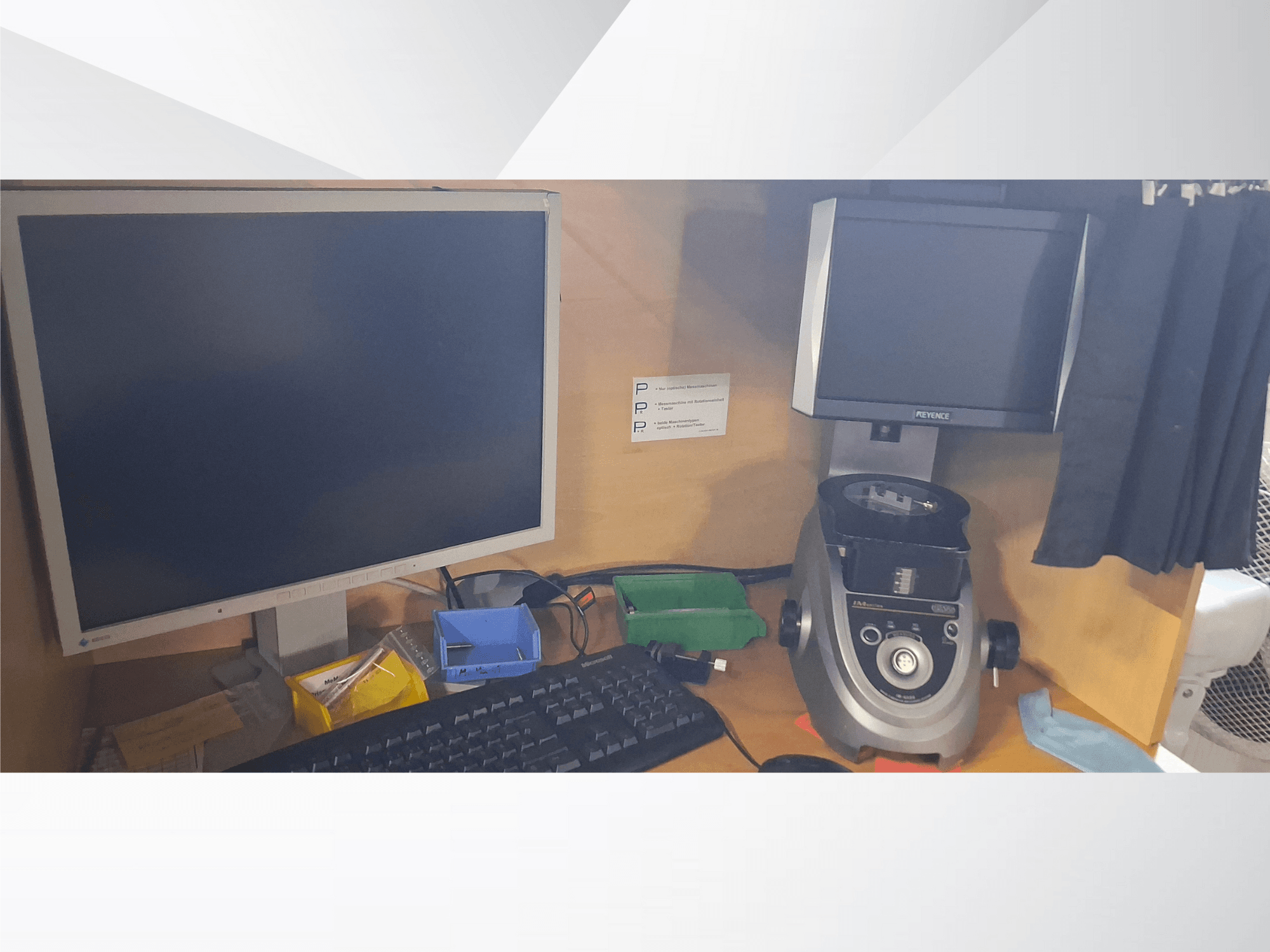 Datora monitors ar tastatūru, PEVA zīmola displejs un pelēka laboratorijas ierīce uz koka galda ar dažādiem paplātēm un papīriem.