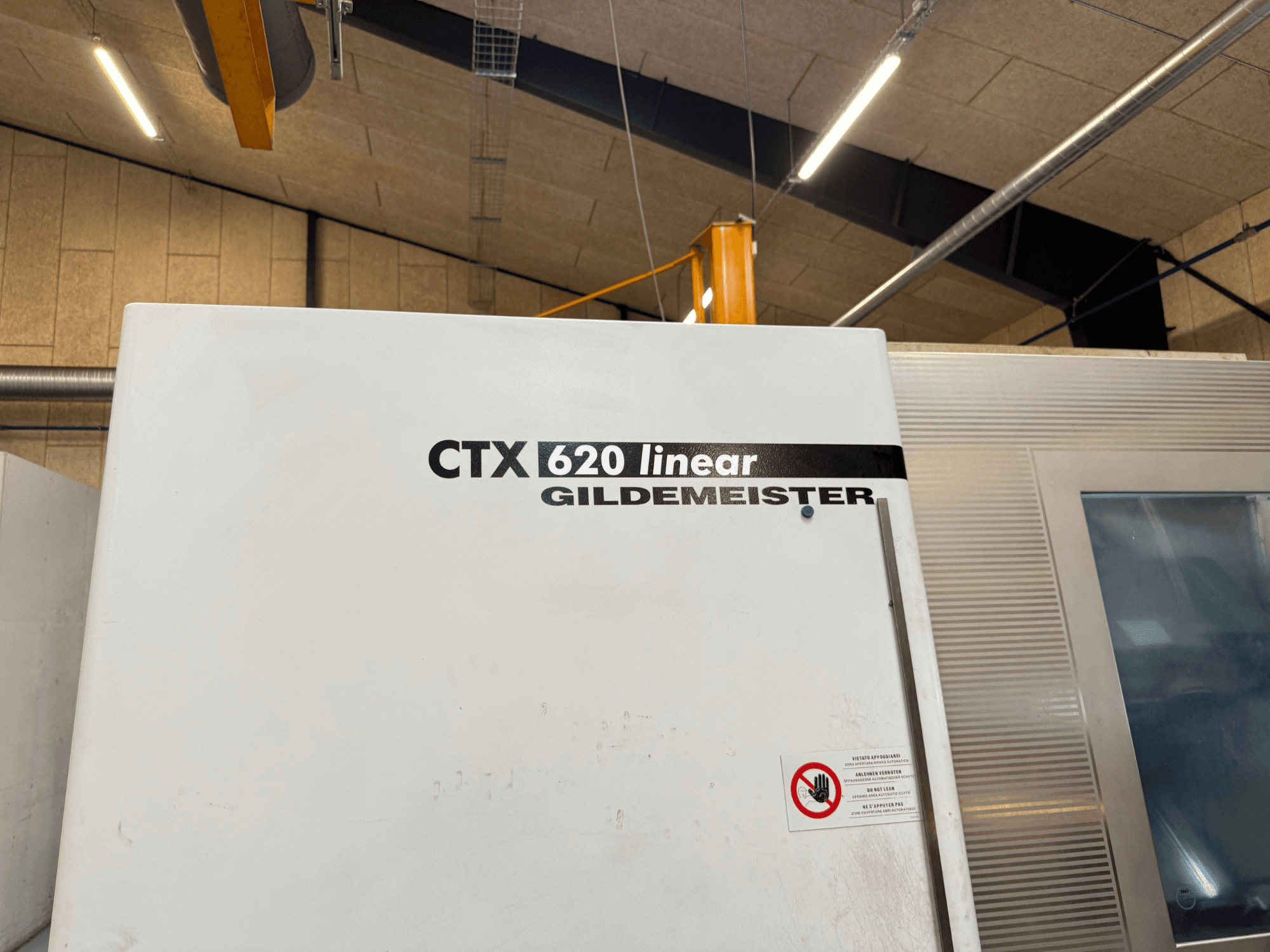 CTX 620 Linear Gildemeister mašīnas skats no sāniem, ar baltu ārējo apdari un drošības brīdinājuma uzlīmes.