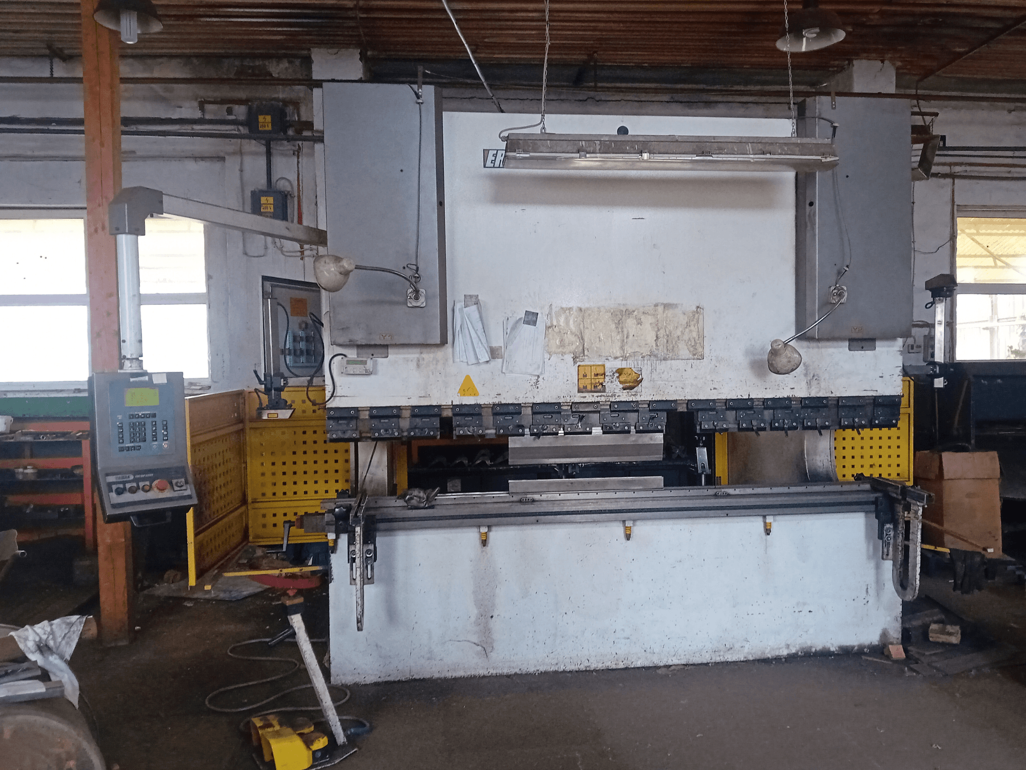 ERMAK CNC HAP 3100x300 hidrauliskā prese ERMAK CNC HAP 3100x300 parādīta priekšpusē, ar vadības paneli un darbagaldu darbnīcā.