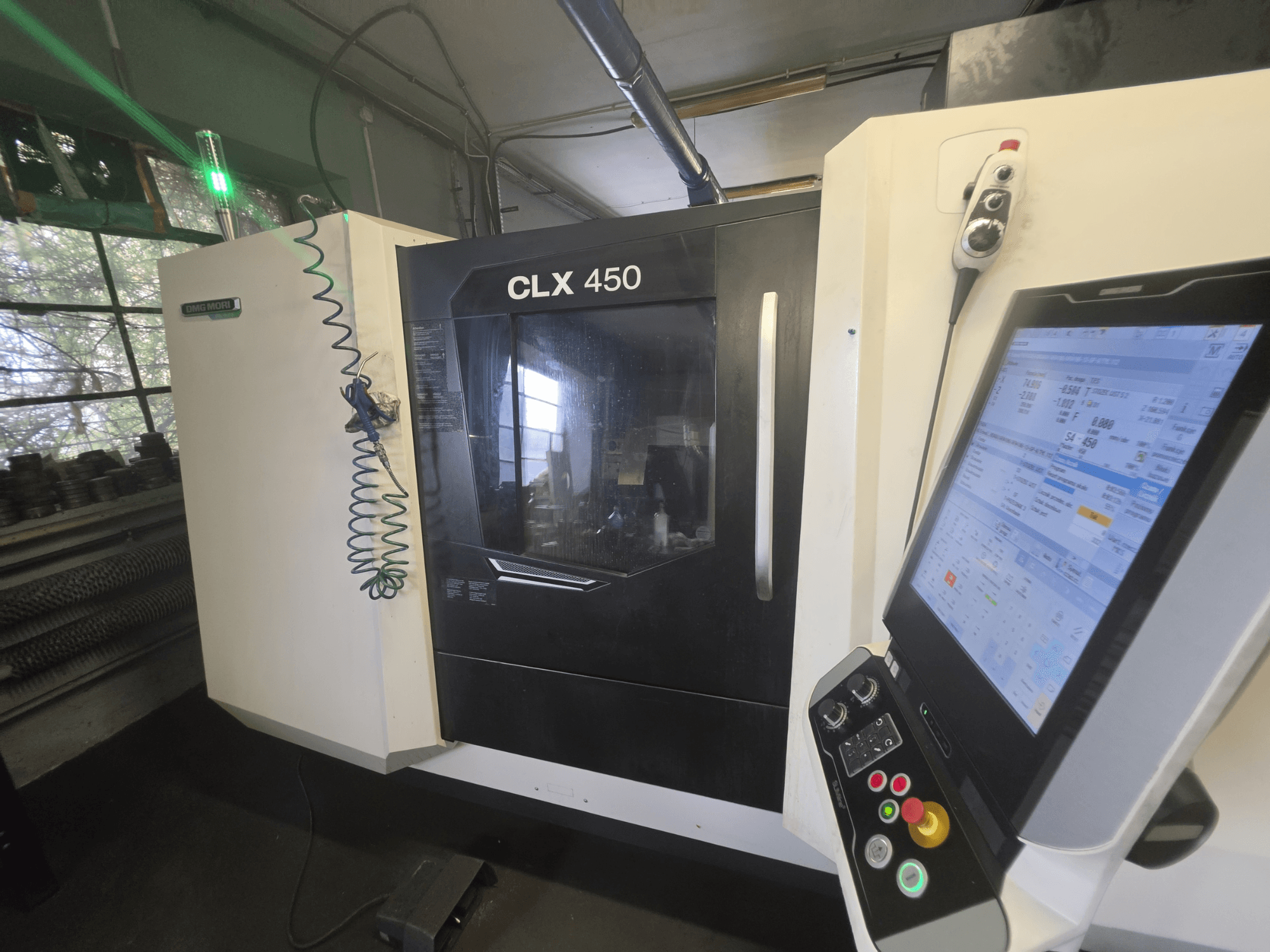 DMG MORI CLX 450 V3 horizontālā virpošanas mašīna, skats no priekšpuses ar vadības paneli un monitoru, kurā tiek parādīti darbības dati.