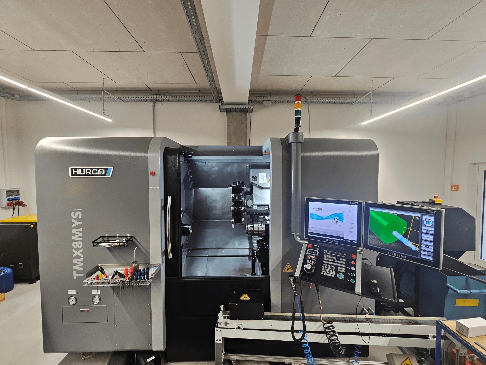 Hurco TMX 8 MYSi frēzēšanas centrs darbnīcā ar diviem monitoriem, vadības paneli un instrumentiem sānos.