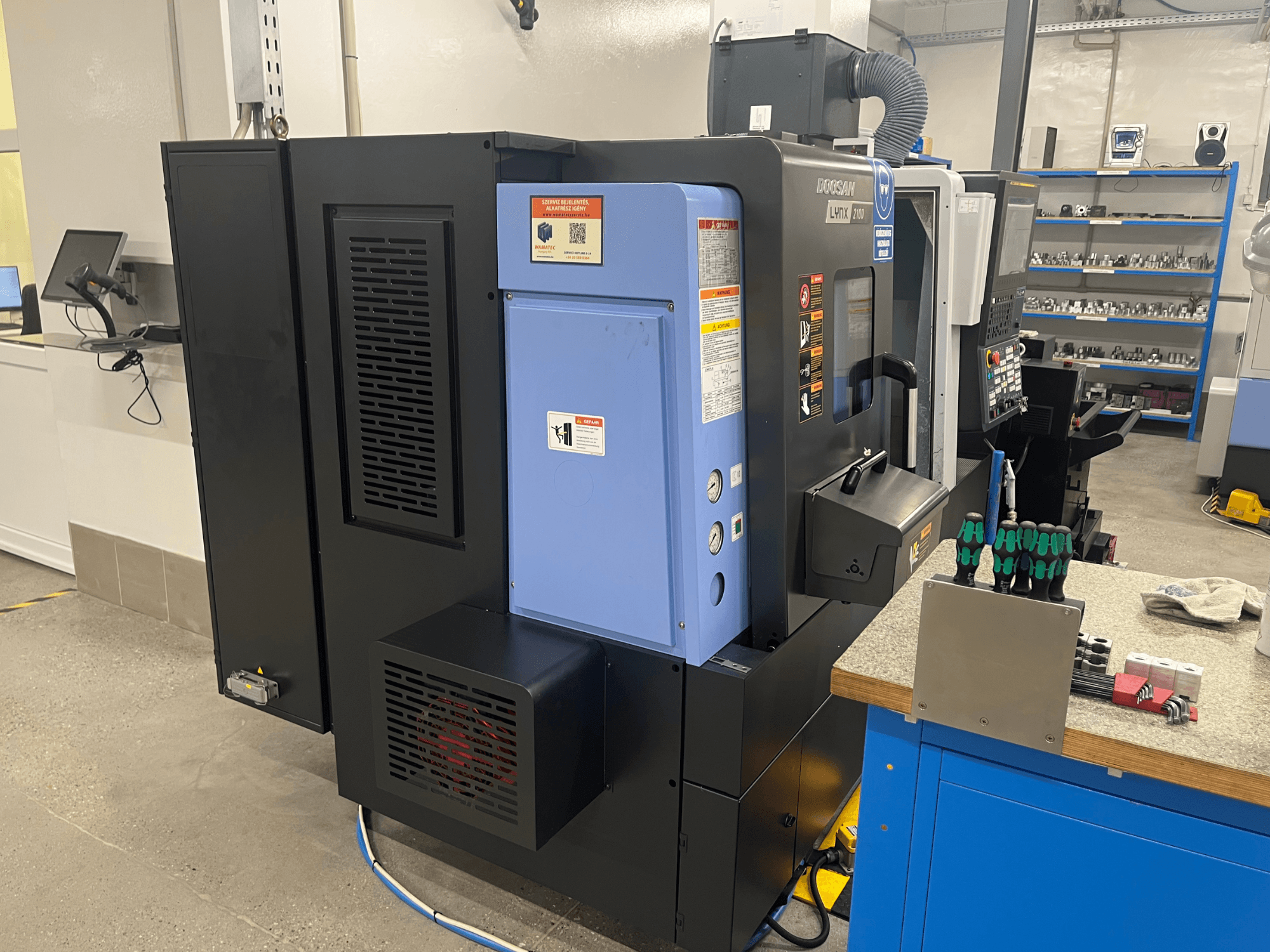 Doosan Lynx 2100 virpa, skats no sāniem, redzams vadības panelis, ventilācijas sistēma un instrumenti uz darbgalda.