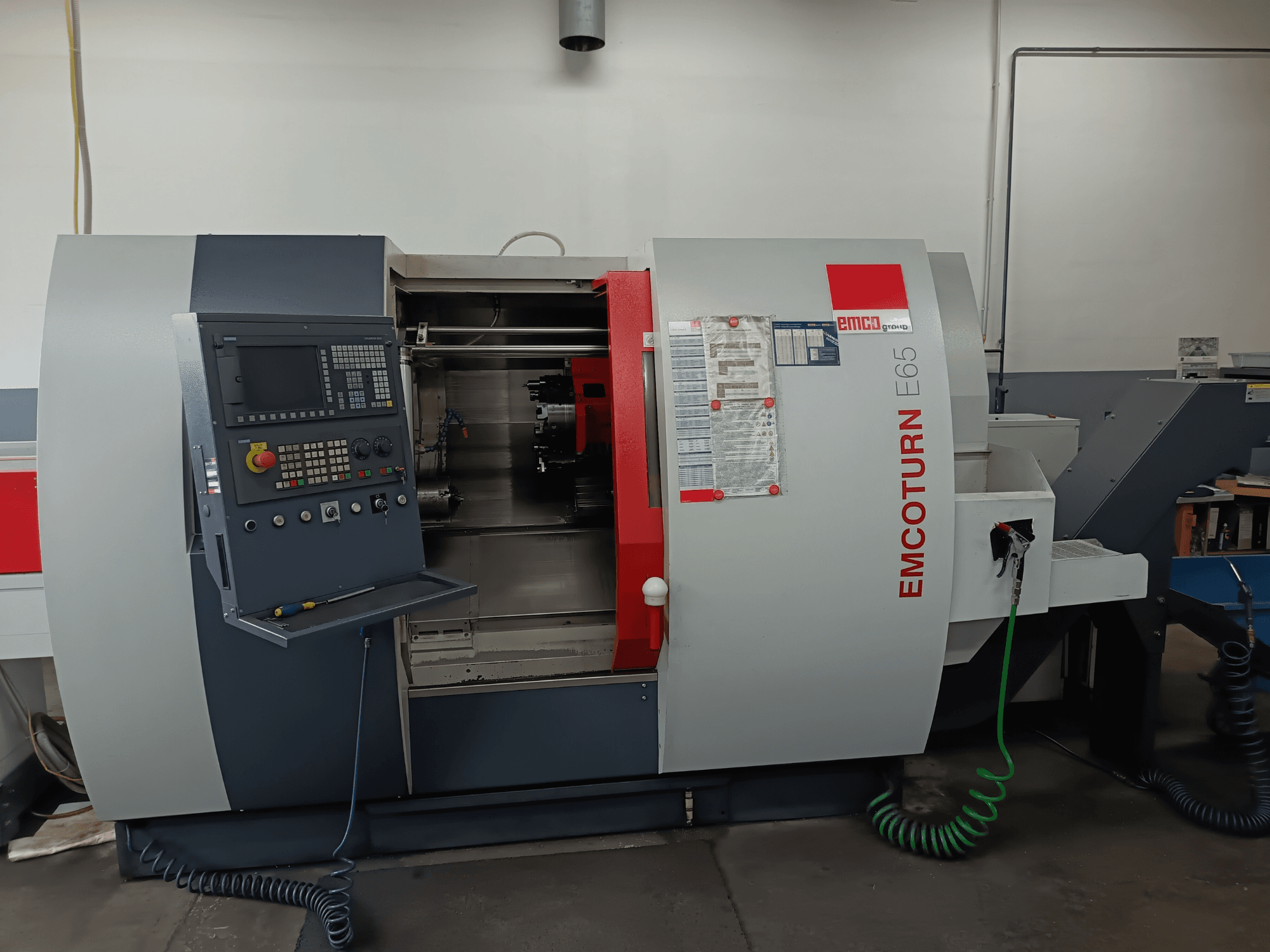 EMCO EMCOTURN E65 rotācijas frēzēšanas centrs, priekšējais skats, kurā redzams vadības panelis, iekšējais mehānisms un funkcijas darbnīcā.