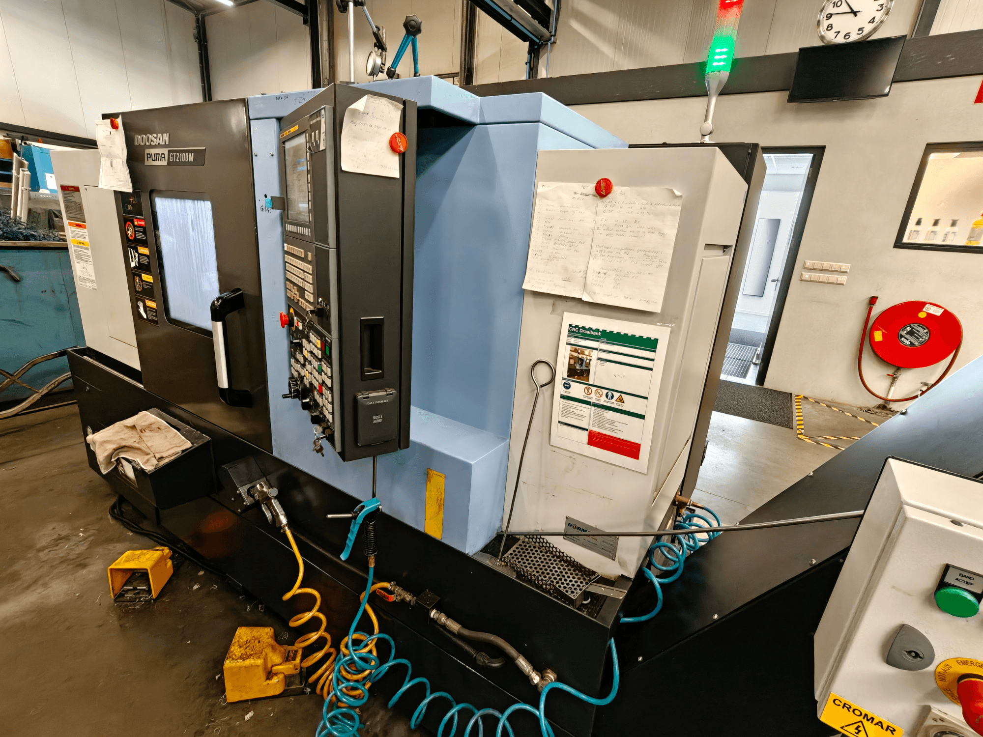 DOOSAN Puma GT 2100M horizontālās virpošanas mašīnas priekšējais skats ar redzamu vadības paneli, drošības elementiem un tehniskās apkopes piezīmēm.