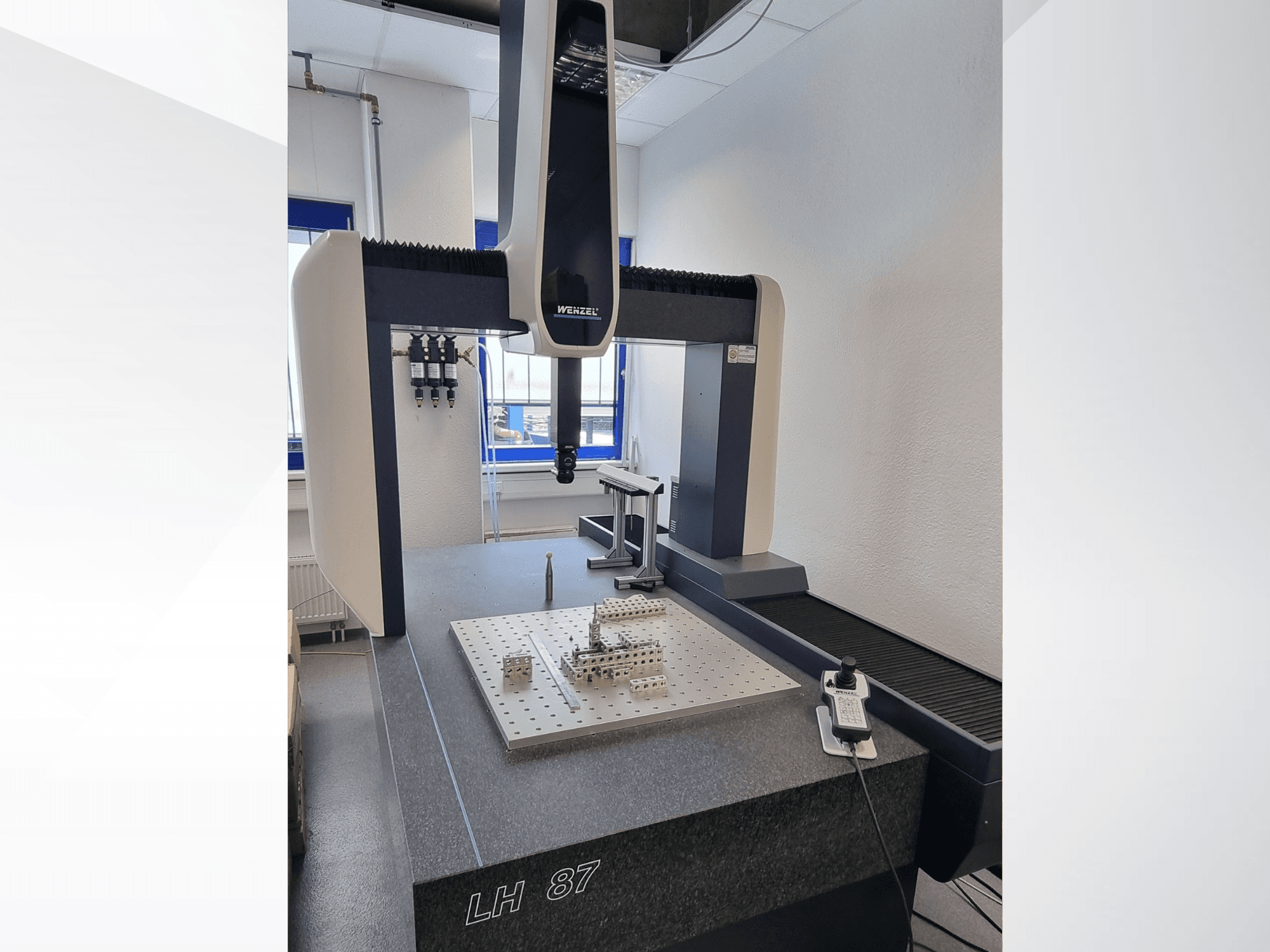 Wenzel LH 87 CMM laboratorijā, skats no priekšpuses, kur redzams mērīšanas zonds virs precīzās virsmas plāksnes un digitālais kontrolieris.