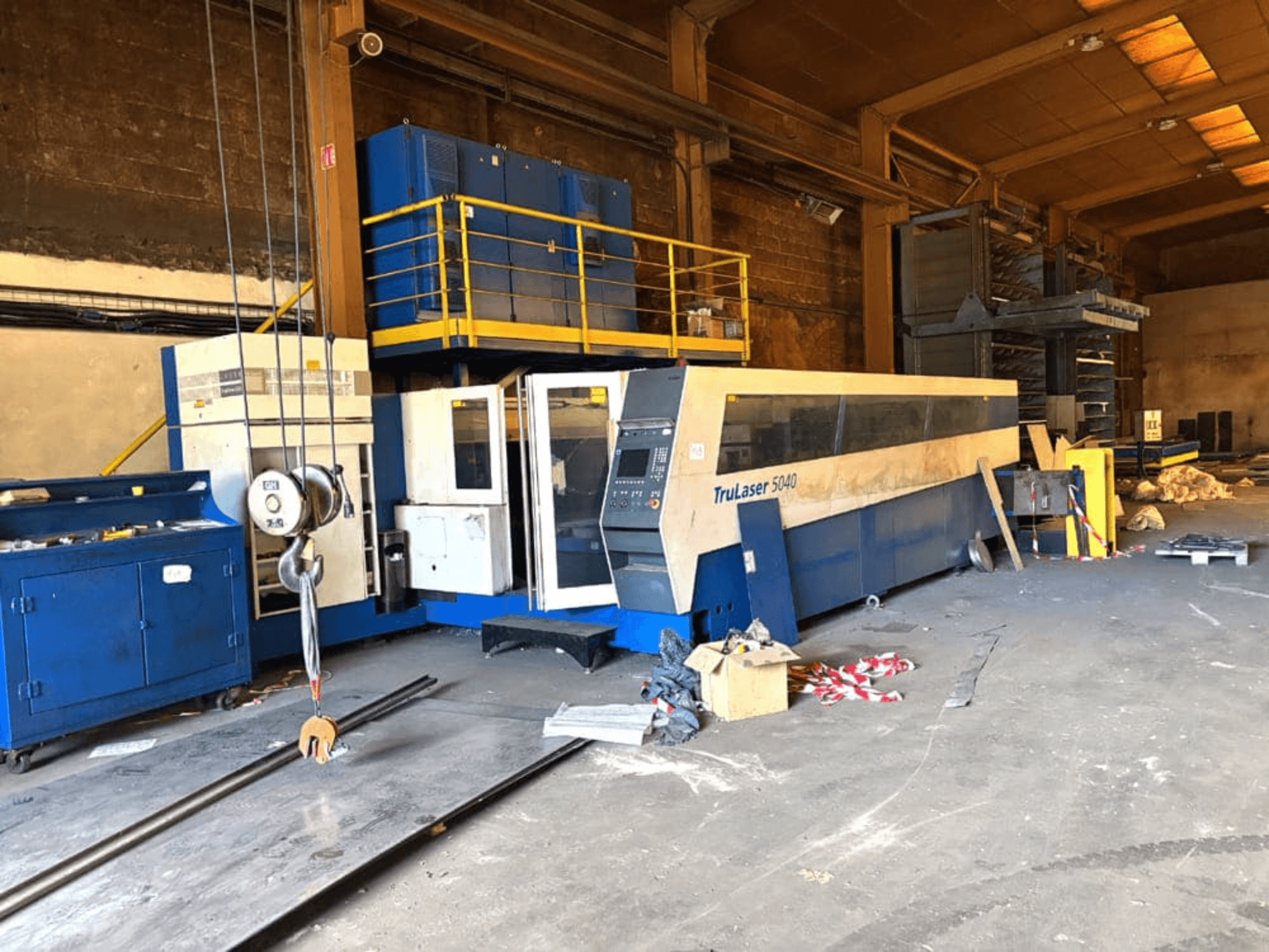 TRUMPF ražota CO2 lāzergriešanas iekārta, modelis TRULASER 5040, attēlota darbnīcā, skats no sāniem ar pārblīvētu fonu.