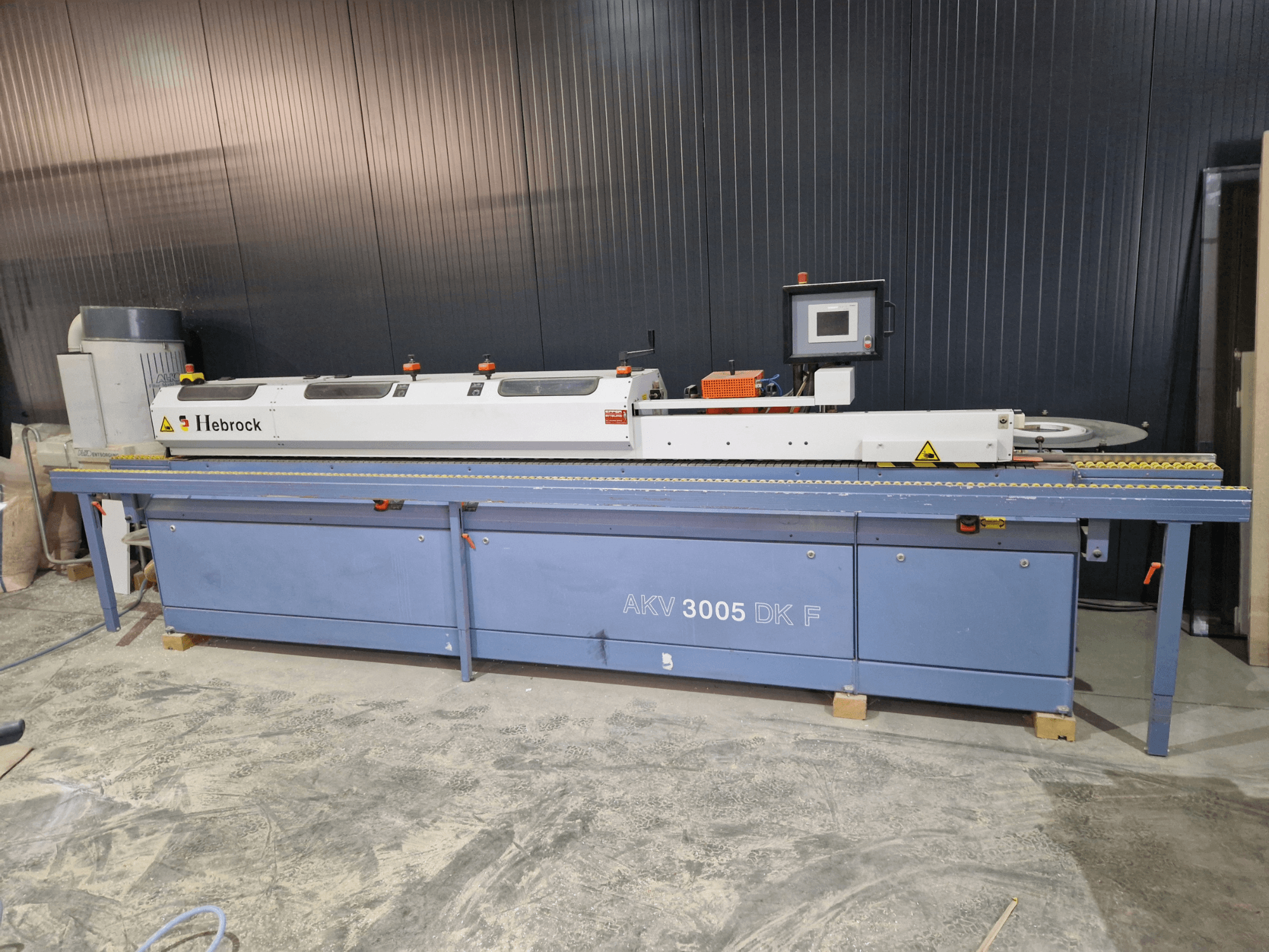 HEBROCK AKV 3005 DK-F malu slīpmašīna, skats no priekšpuses, ar vadības paneli, padeves lenti un regulējamiem iestatījumiem.