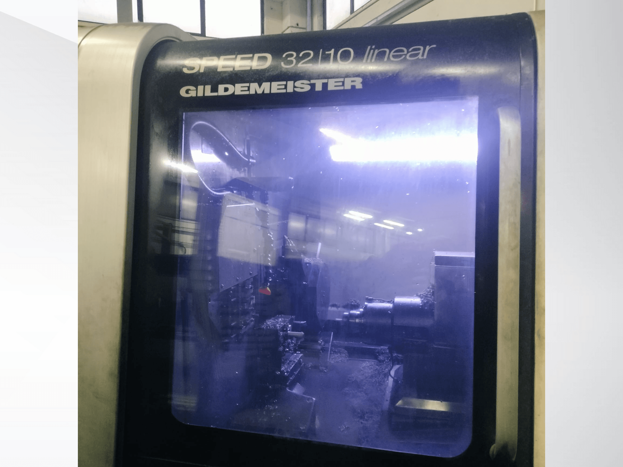 Gildemeister SPEED 3210 lineārās CNC mašīnas priekšējais skats, kurā redzami iekšējie komponenti un šķidrais dzesēšanas šķidrums darbībā.