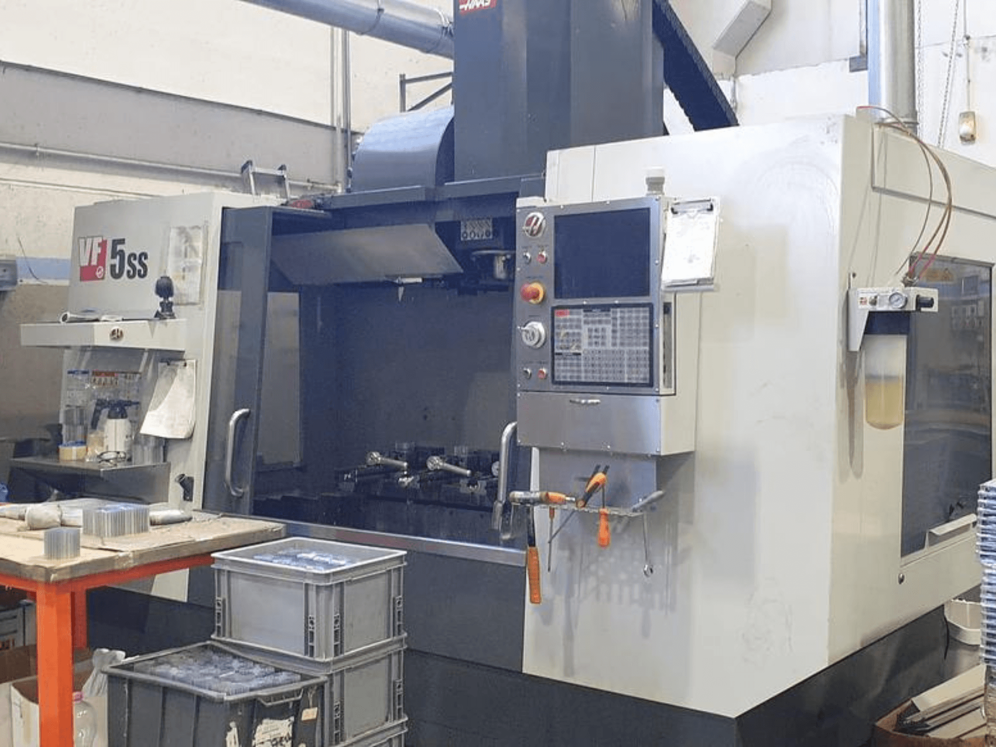 HAAS VF-5SS vertikālais apstrādes centrs priekšpusē, kurā redzams vadības panelis, darba vieta un glabāšanas tvertnes.