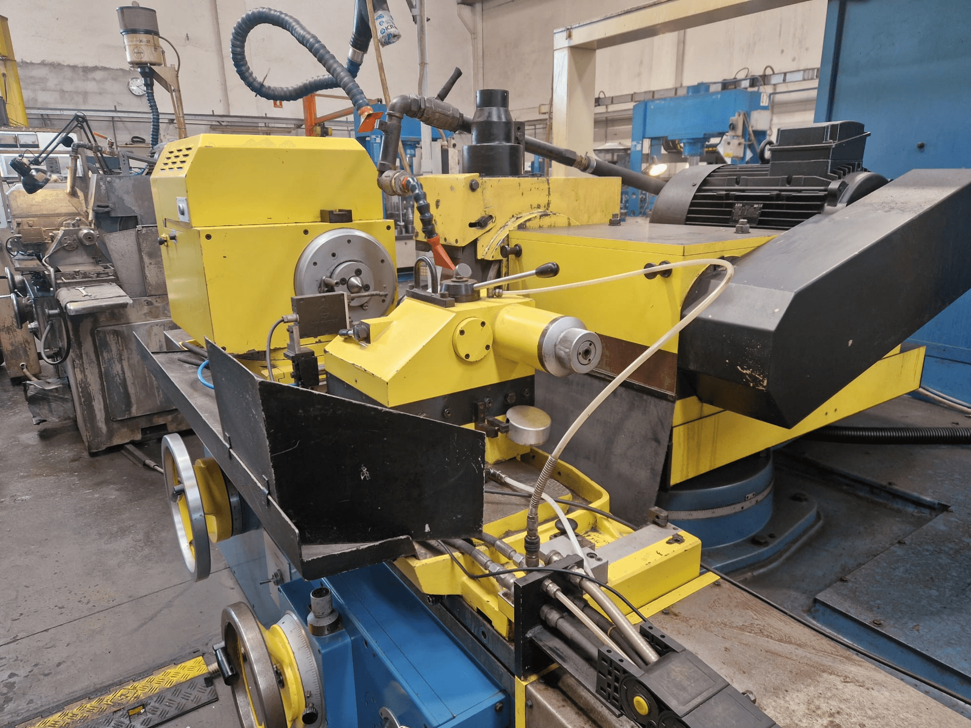 Dzeltena rūpnieciska mašīna ar melnu daļu, ar ciparnīcu un šļūtenēm, skatīta no priekšpuses nelielā leņķī.
