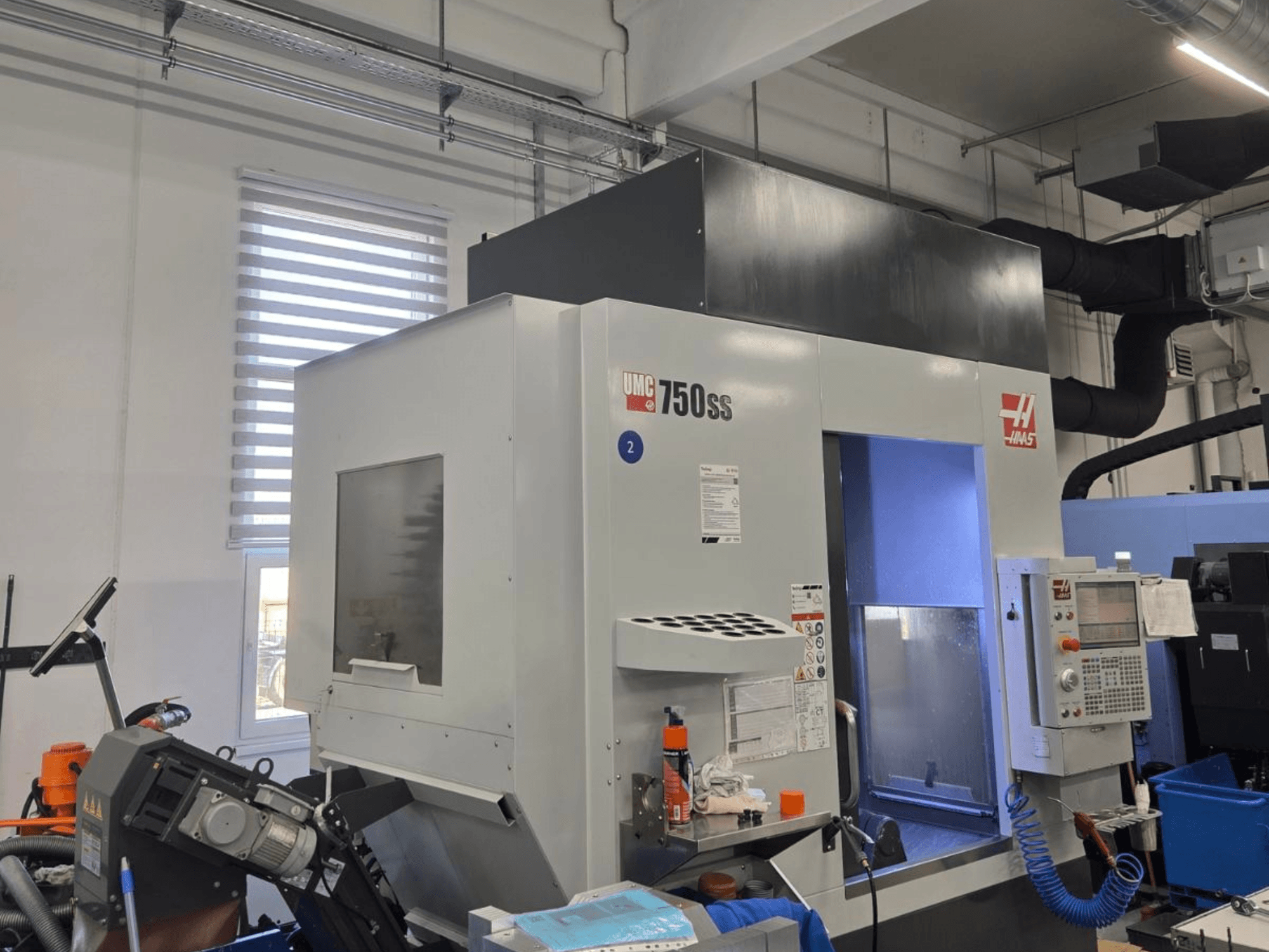 Haas UMC-750SS vertikālais apstrādes centrs, skats no priekšpuses, ar vadības paneli un brīvu piekļuvi apstrādes zonai.
