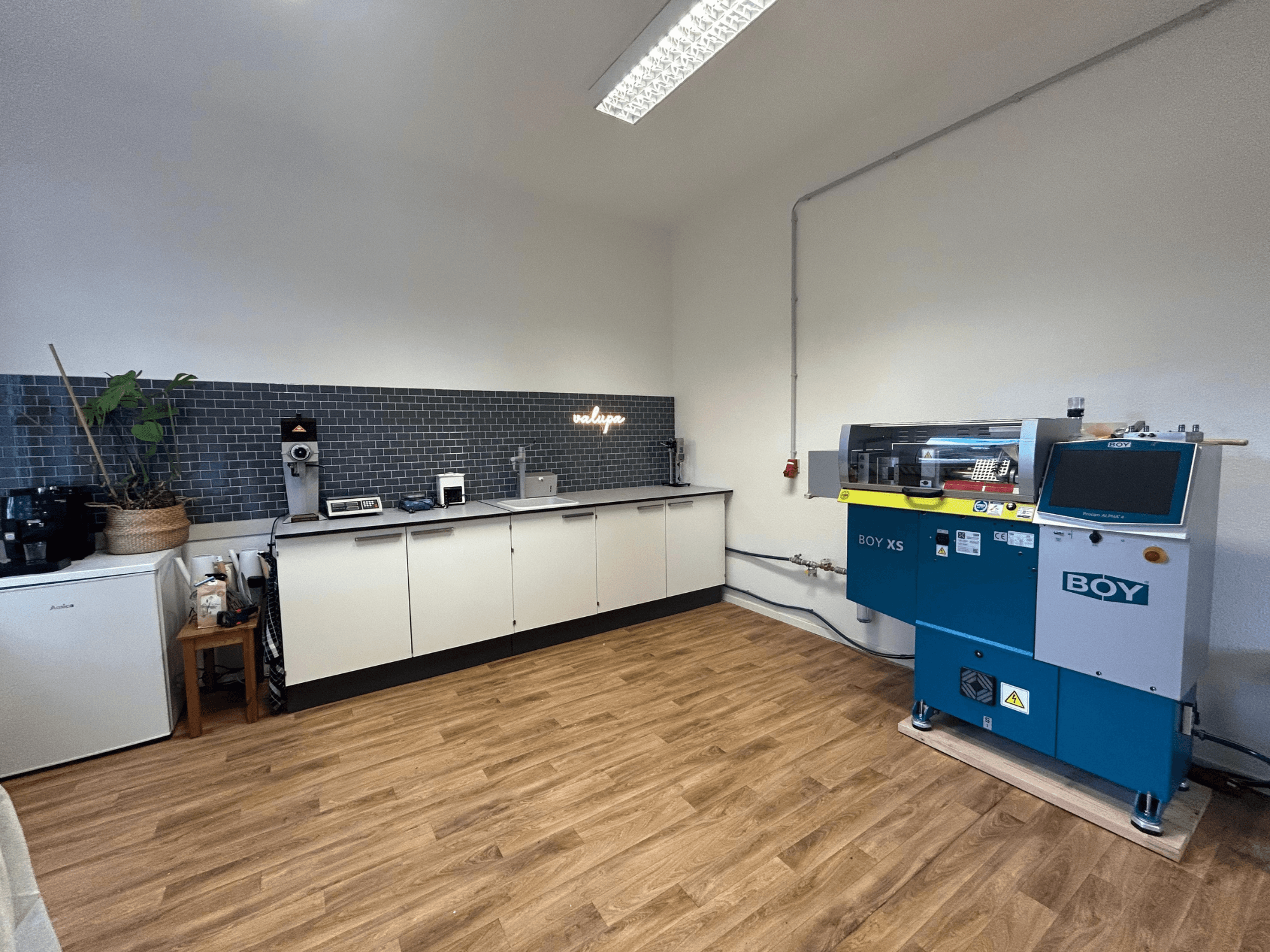 Hidrauliskā iesmidzināšanas iekārta BOY XS 161, skats no priekšpuses, modernā virtuvē ar iekārtām un koka grīdas segumu.