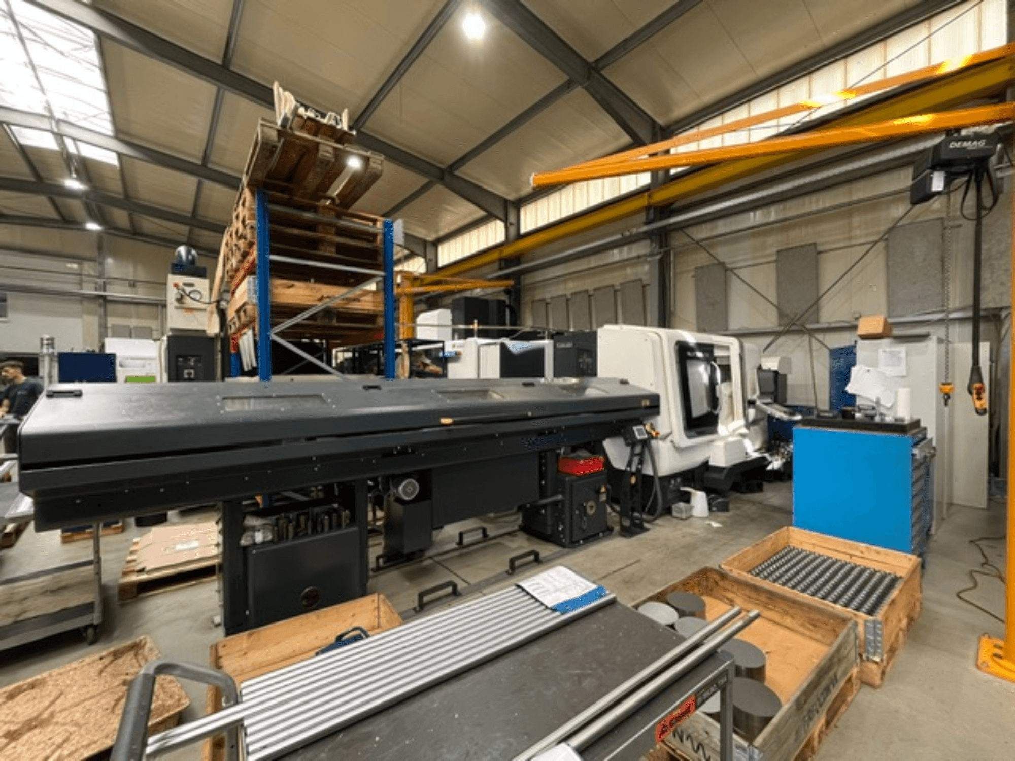 DMG MORI MORI NLX 2500/700 SY horizontālā virpošanas mašīna rūpnīcas vidē, skats no sāniem, redzami darbarīki un paletes.