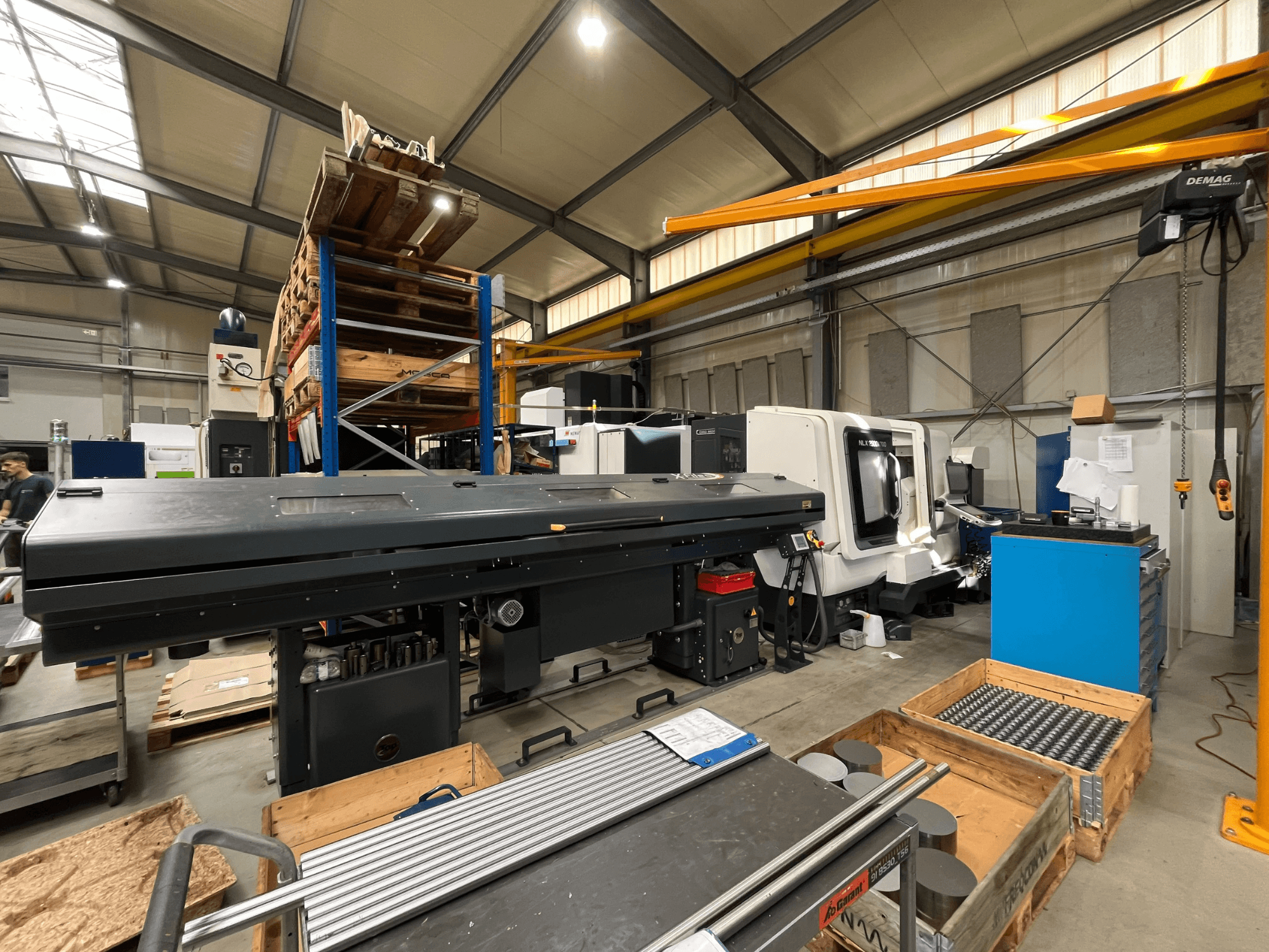DMG MORI MORI NLX 2500/700 SY horizontālā virpošanas mašīna darbnīcā, skats no sāniem, fonā redzama noliktava un darbarīki.