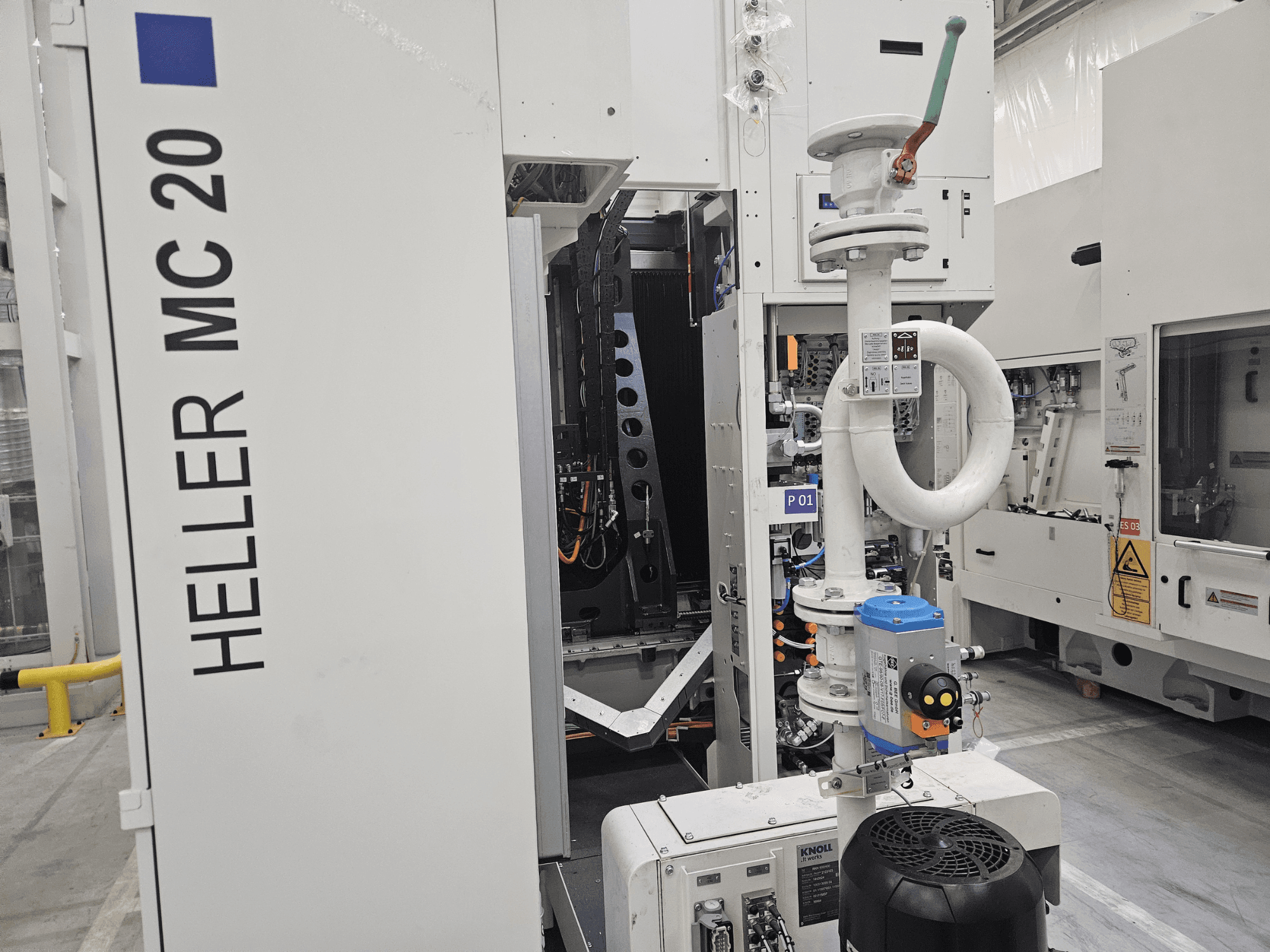 Heller MC 20 mašīna rūpnīcā, kurā redzams vadības panelis un mehāniskās sastāvdaļas no sānu skata.