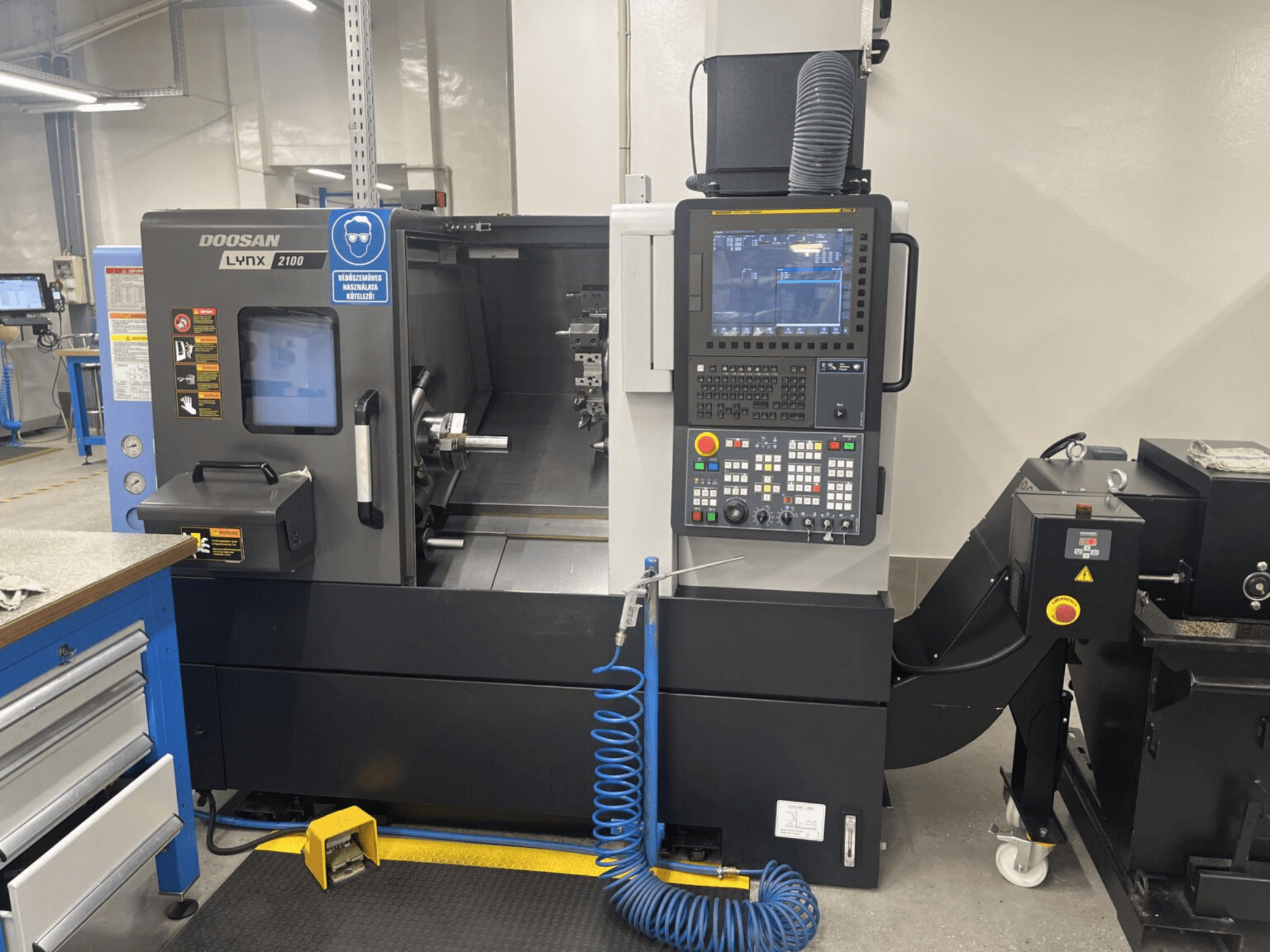 DOOSAN Lynx 2100A horizontālās virpošanas mašīnas priekšējais skats, kurā redzams vadības panelis un vārpstas zona ar ievērojamām drošības funkcijām.