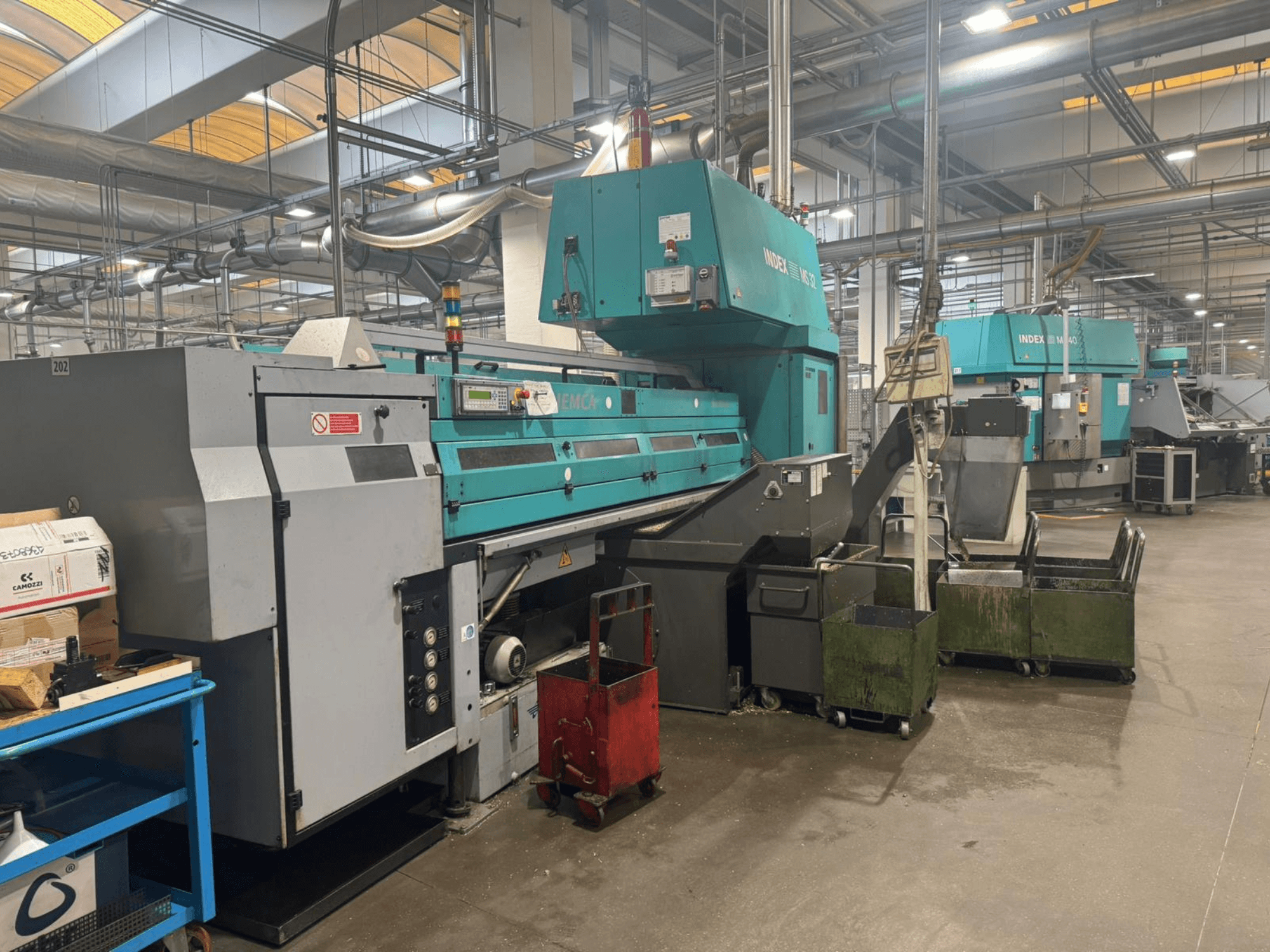 Daudzvārpstu virpošanas mašīna INDEX MS32C, priekšējais skats, kurā redzamas vadības ierīces un darba zona darbnīcā.