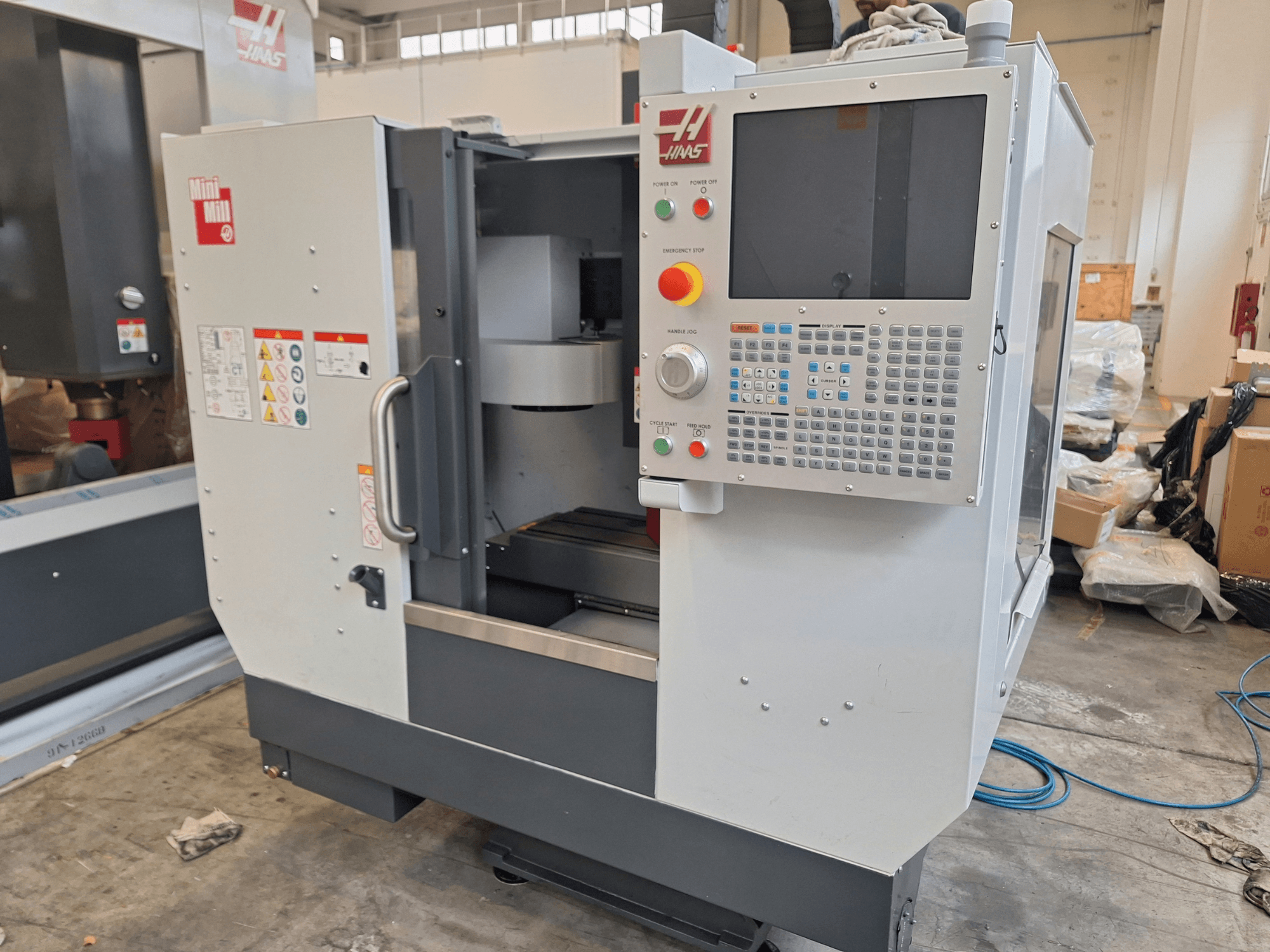 Vertikālais apstrādes centrs „HAAS Mini Mill“ no priekšpuses, kurā redzams vadības panelis ar pogām un displeju.