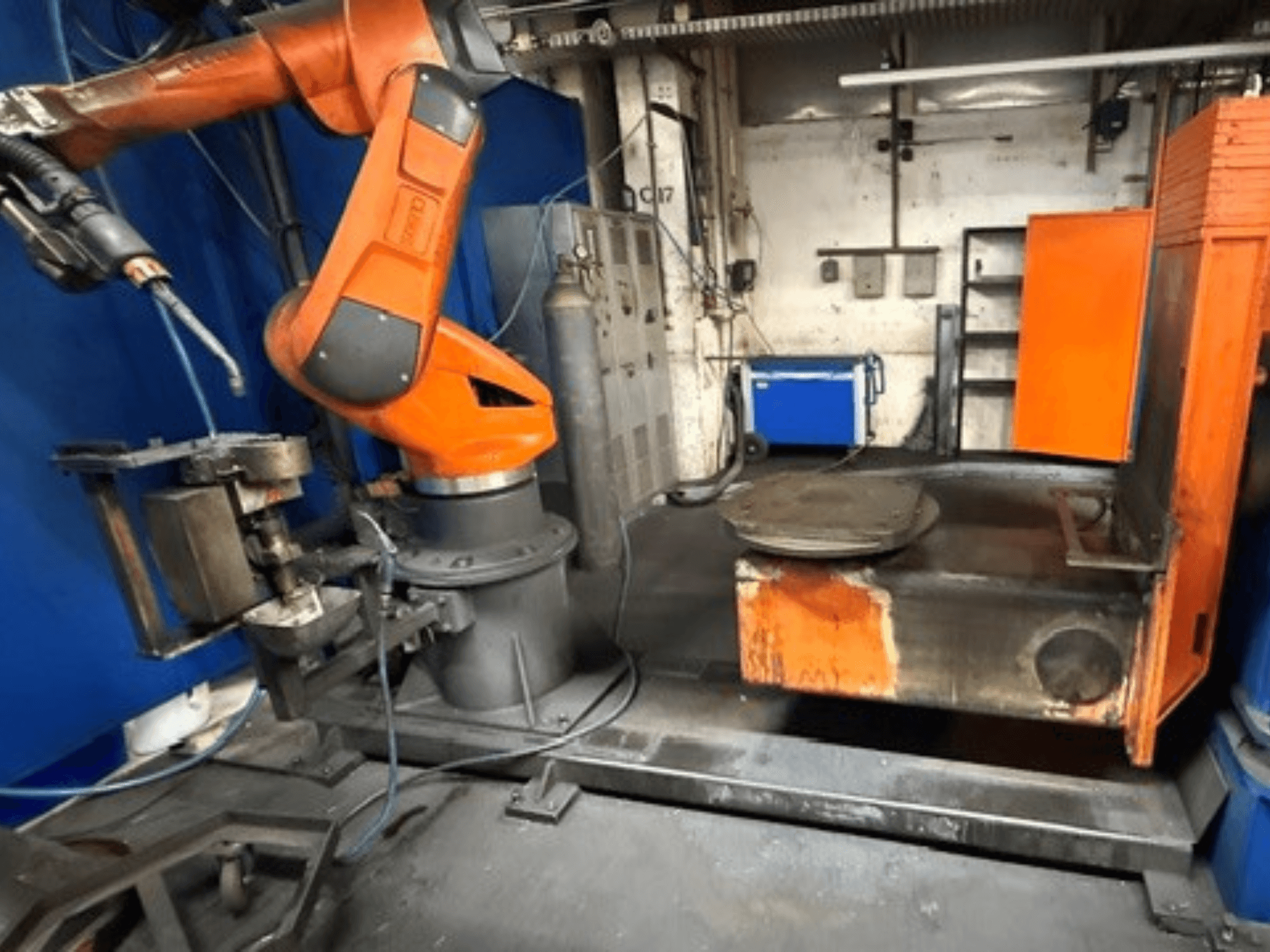 CLOOS C50 metināšanas robots, skats no priekšpuses, ar oranžu robota roku un metāla darba galdu.
